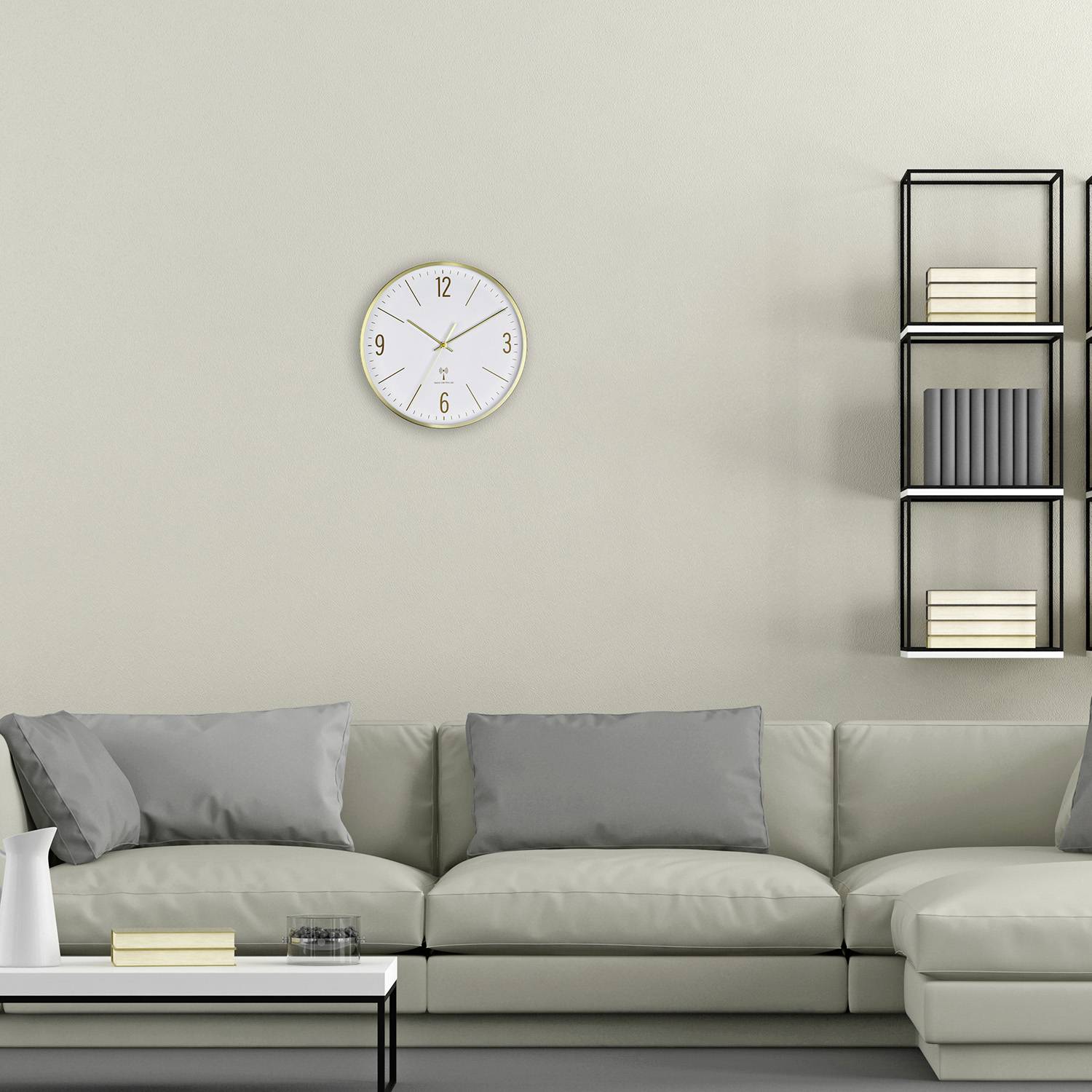 Wohnzimmer mit grauem Sofa, weißen Kissen, weißem Tisch, dekorativer Uhr an der Wand und Regal mit Büchern.
