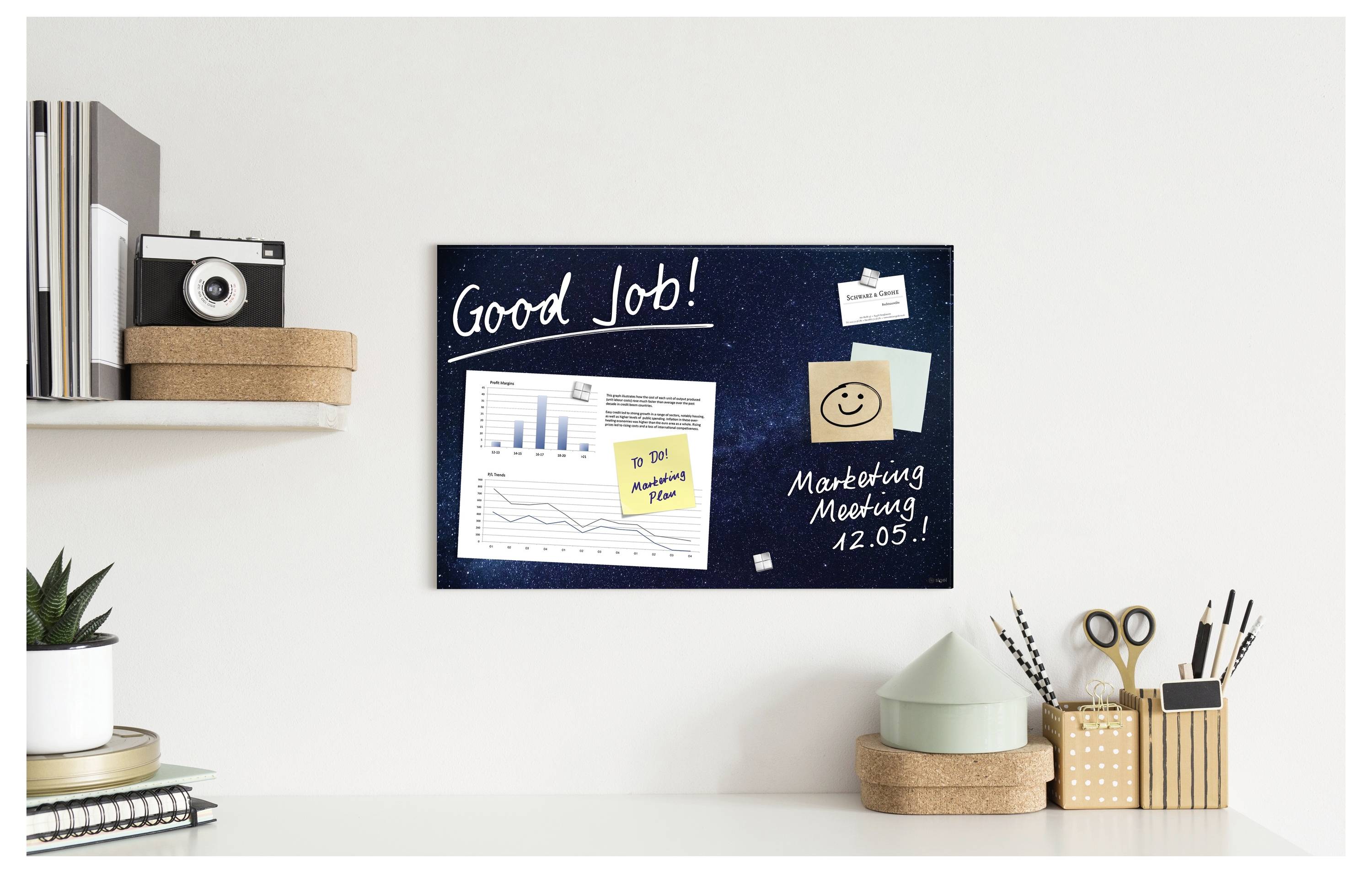Homeoffice-Schreibtisch mit einer Wandtafel, auf der „Gut gemacht!" steht, daneben Diagramme, eine Haftnotiz und „Marketing-Treffen 12.05!" handschriftlich darunter geschrieben.