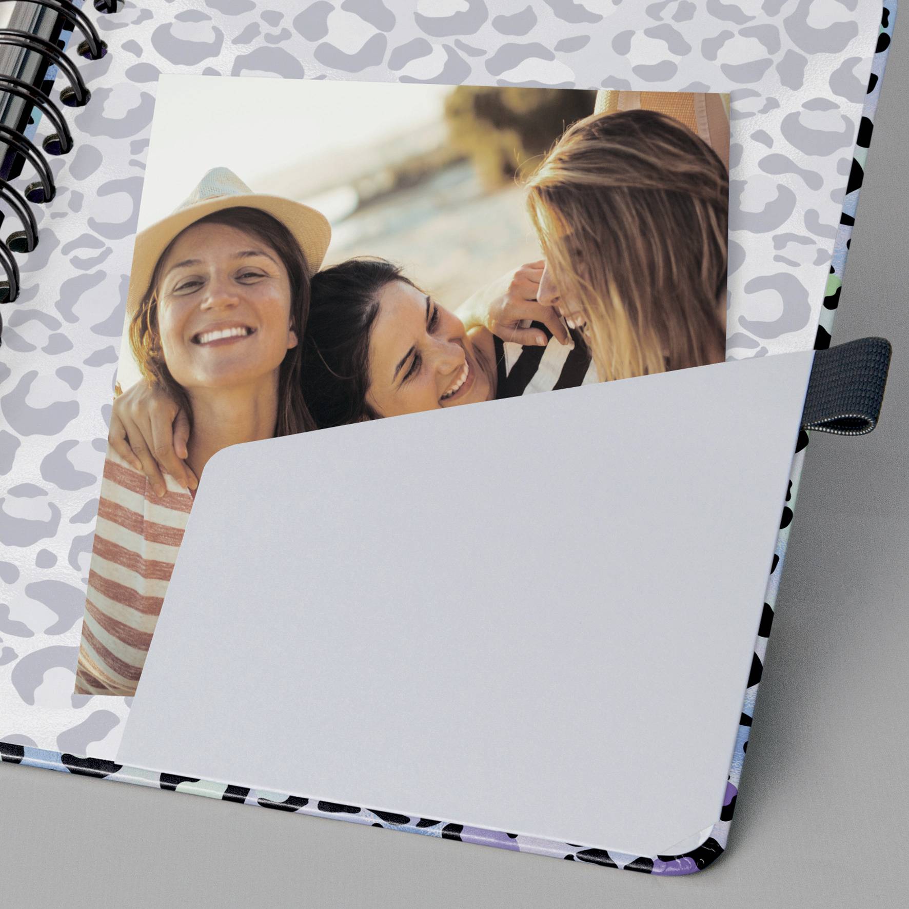 Drei fröhliche Frauen machen ein Selfie am Strand. Eine trägt einen Hut. Das Bild ist in ein Notizbuch mit Leopardenmuster eingeheftet.