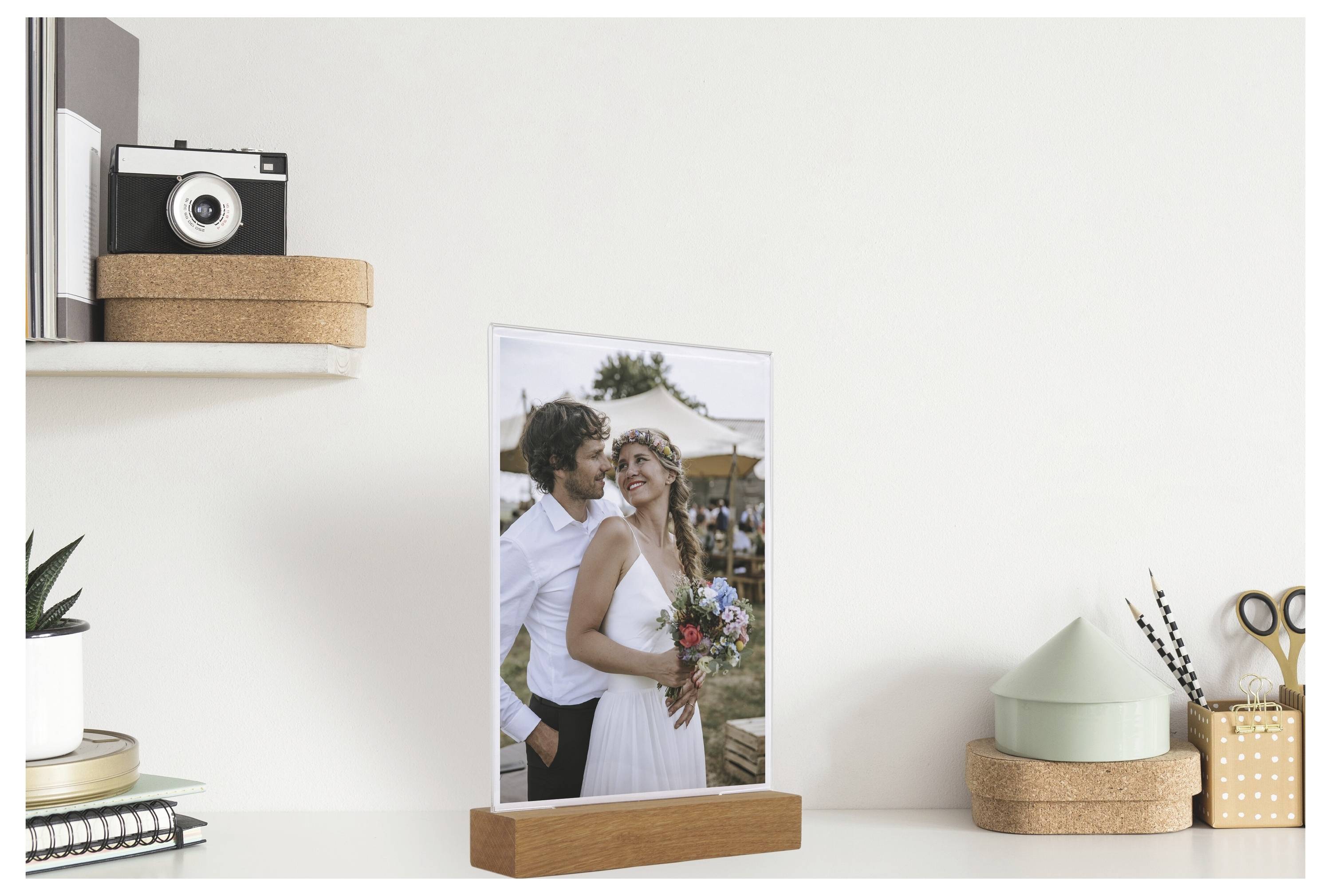Gerahmtes Hochzeitsfoto eines lächelnden Paares auf einem weißen Schreibtisch, mit dekorativen Regalen, Pflanzen und Schreibwaren rundherum.