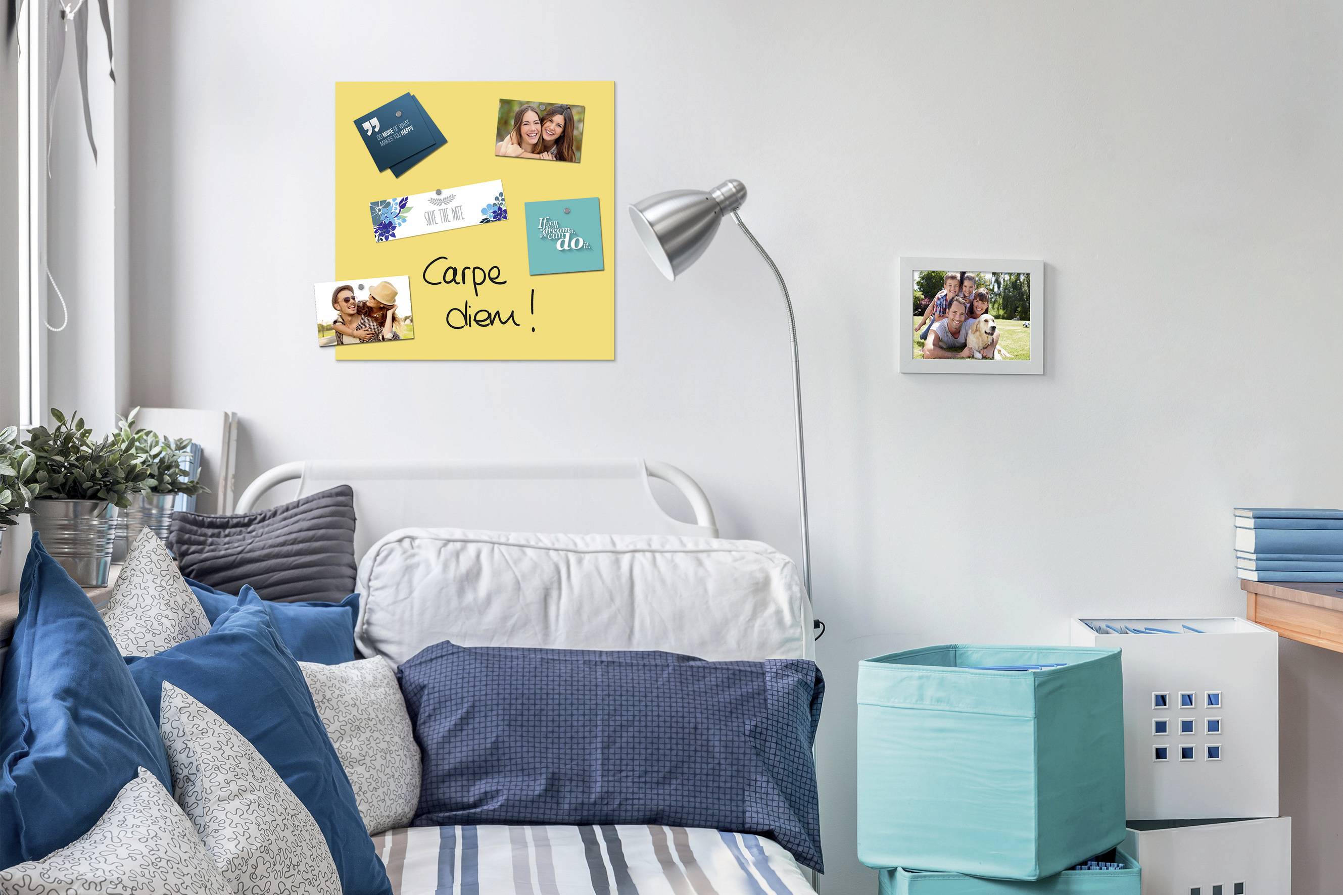 Zimmer mit einem Bett, dekoriert mit blauen Kissen. An der Wand ein Plakat mit Fotos und der Aufschrift 'Carpe diem!'.