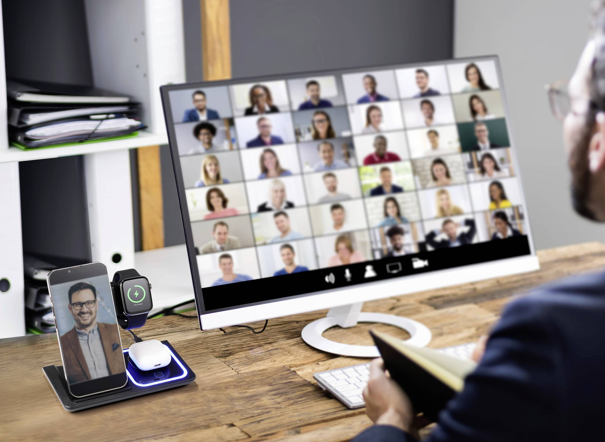 Eine Person nimmt an einer Videokonferenz mit vielen Teilnehmern auf einem Computerbildschirm teil. Ein Handy zeigt denselben Anruf.
