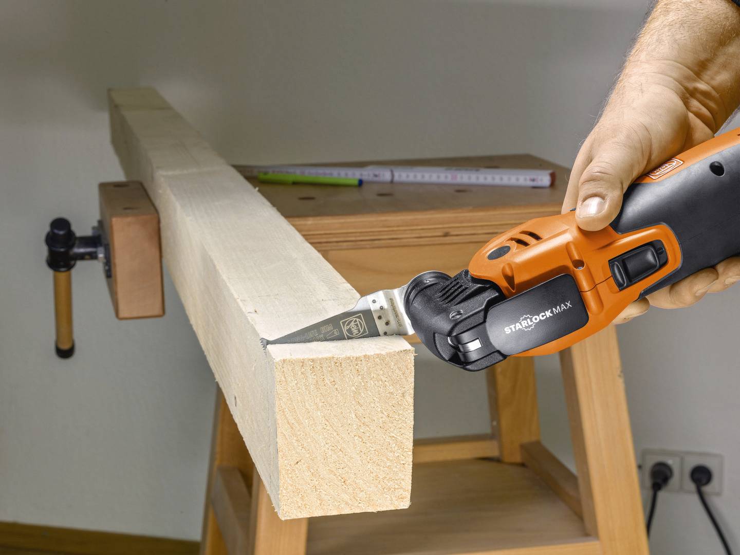 Eine Person schneidet mit einem oszillierenden Multifunktionswerkzeug ein Stück Holz auf einer Werkbank.