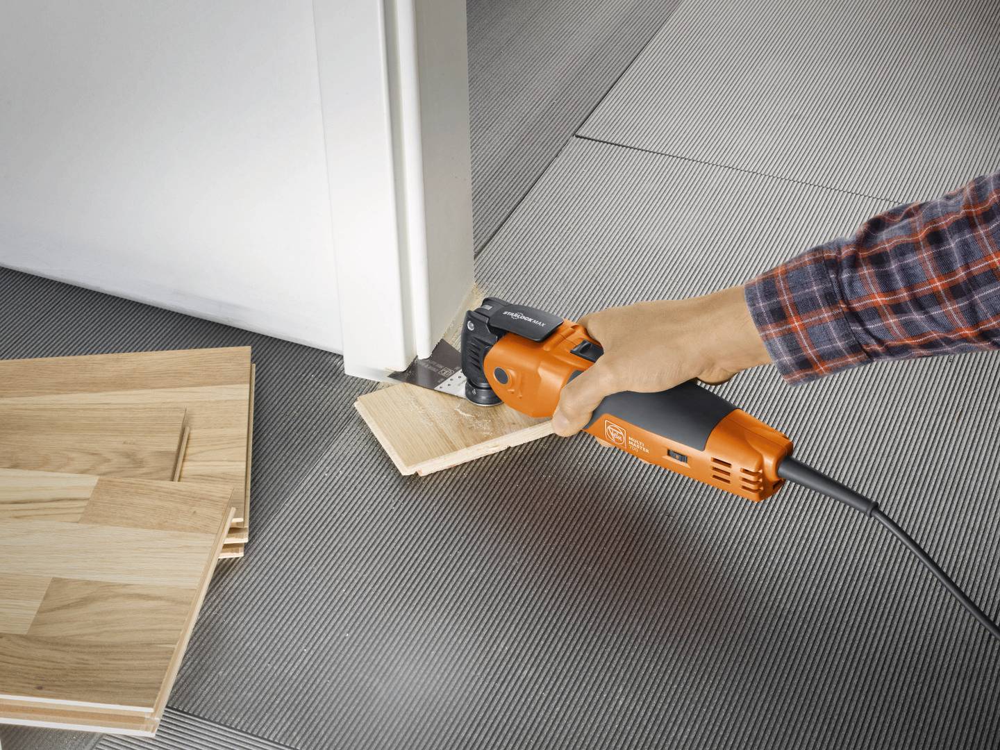 Eine Person schneidet mit einem Elektrowerkzeug ein Holzstück an einer Türzarge. Daneben liegen weitere Holzstücke.