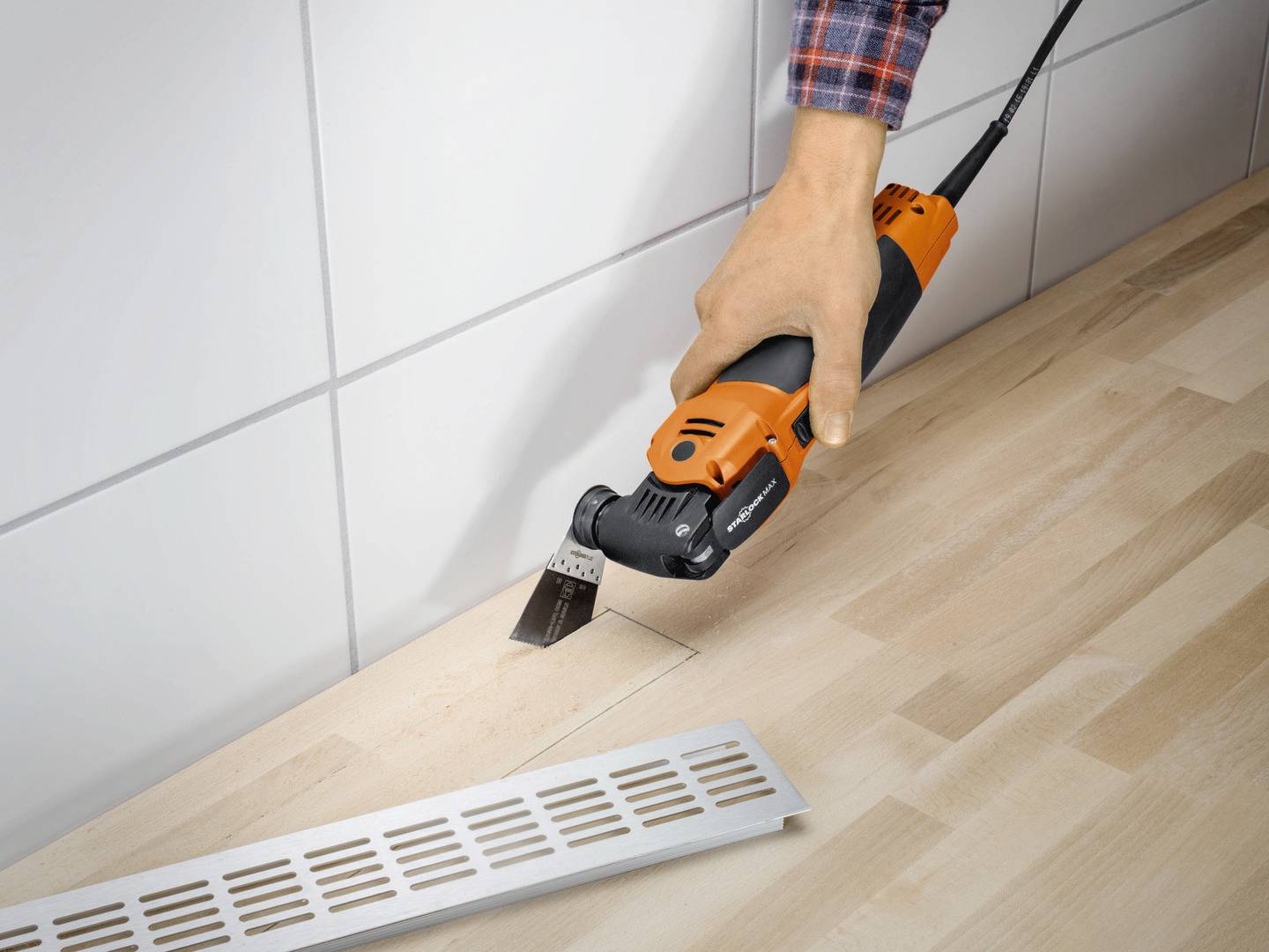 Eine Person schneidet präzise eine rechteckige Öffnung in eine Holzfläche mit einem oszillierenden Multitool. Ein Lüftungsgitter liegt daneben.