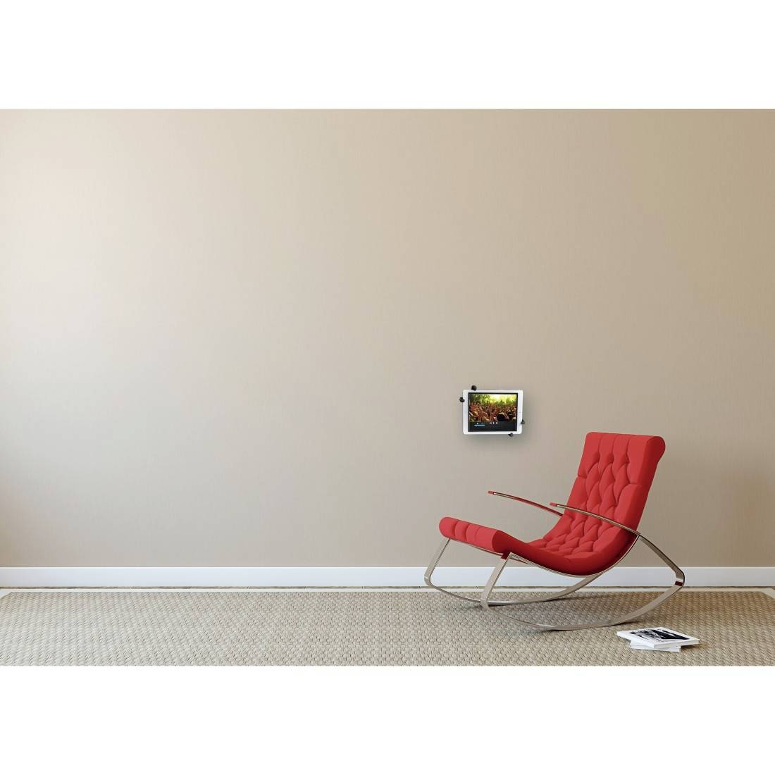 Ein roter Schaukelstuhl steht in einem minimalistischen Raum mit beigefarbenen Wänden. An der Wand hängt ein kleines, hell beleuchtetes Kunstwerk.