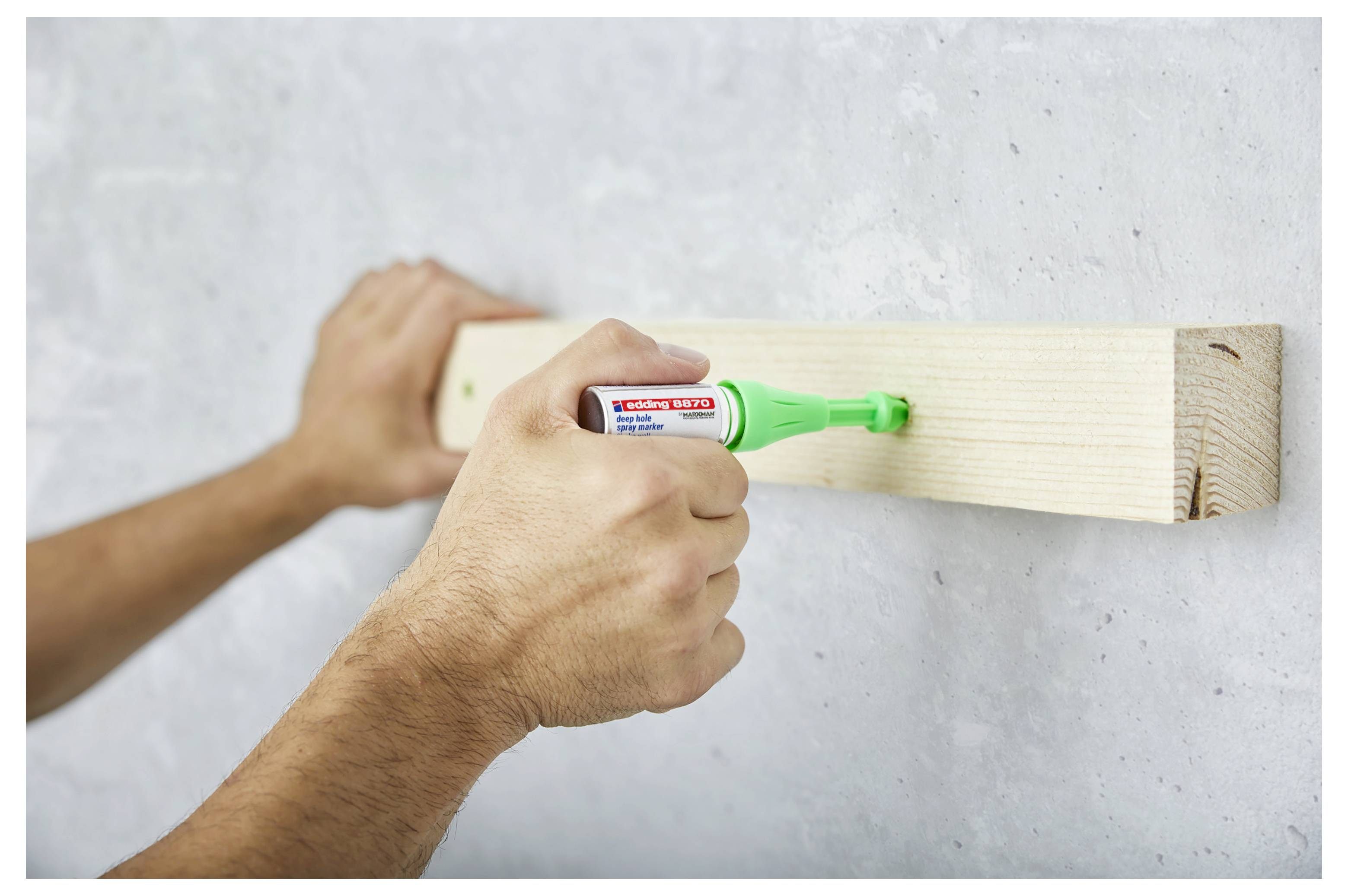 Hände, die mit einem grünen Marker eine Holzplatte an einer Wand markieren, als würden sie für die Installation messen oder beschriften.