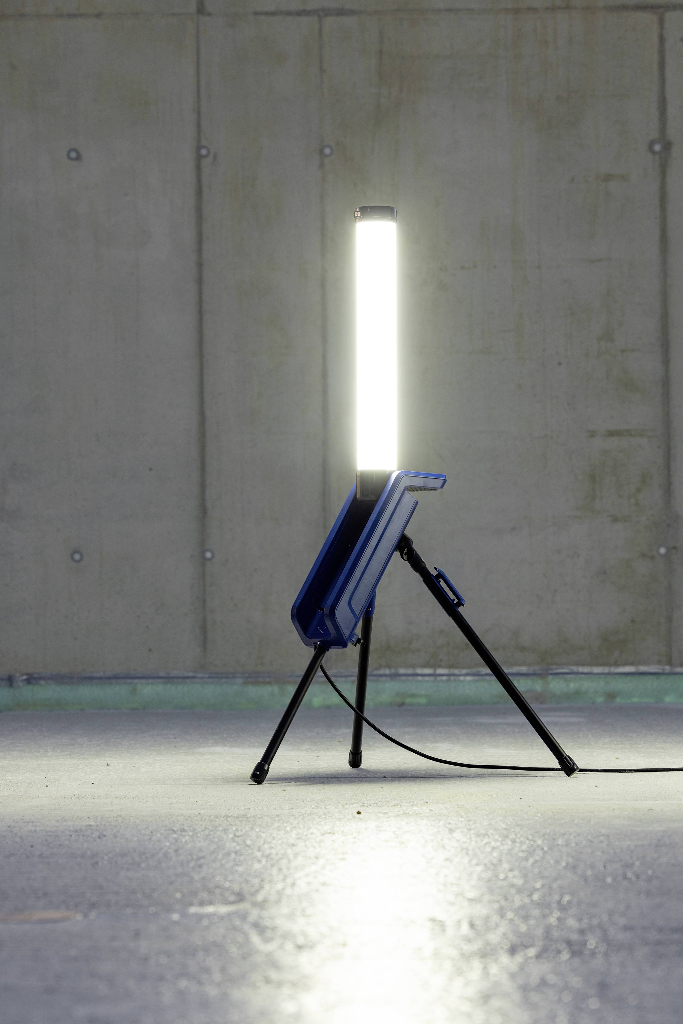 Ein leuchtender Stab auf einem Stativ steht in einem leeren Raum mit Betonwänden. Das Licht strahlt hell und gleichmäßig.