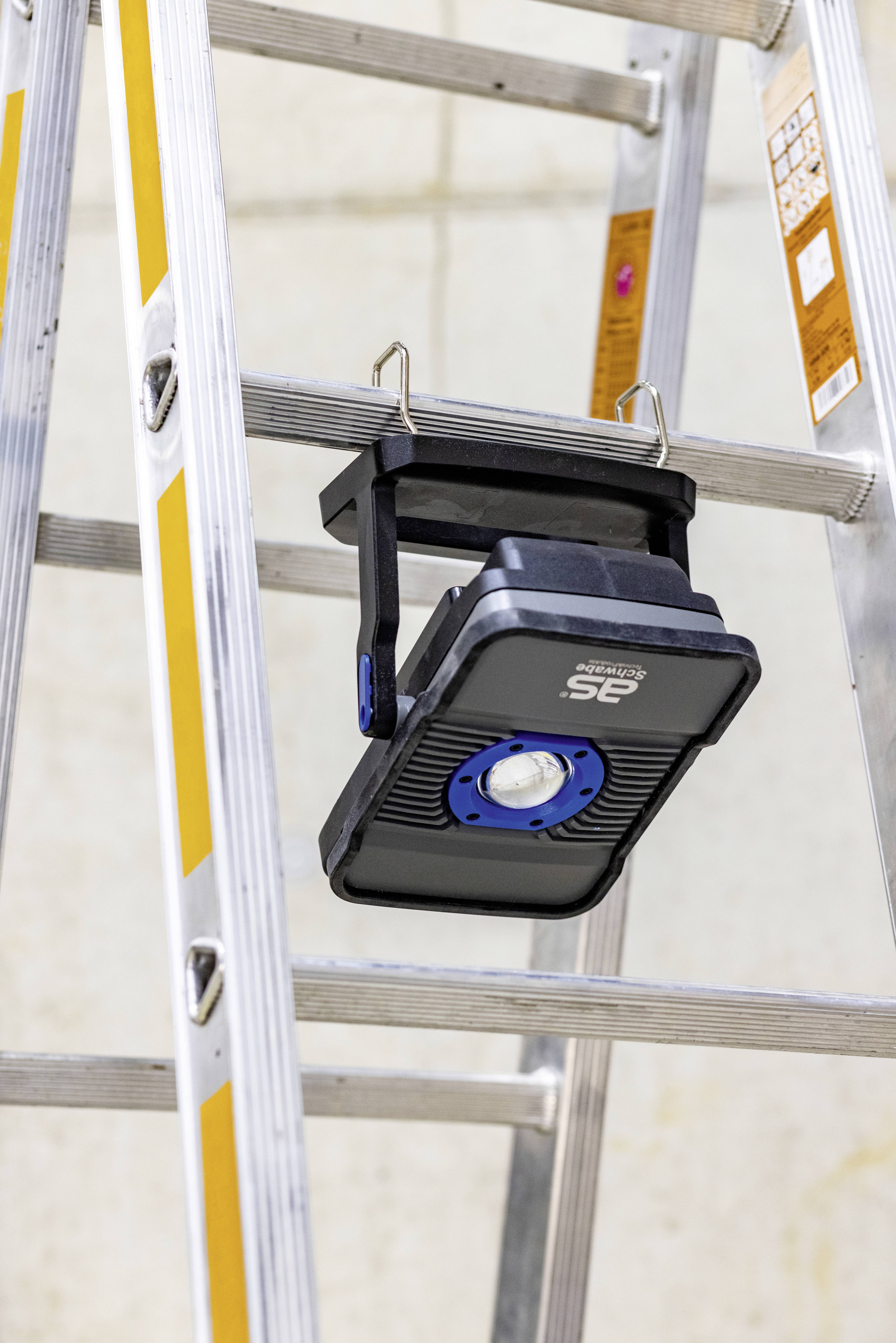 Eine tragbare LED-Arbeitsleuchte hängt an einer Leiter, beleuchtet eine Arbeitsfläche, um Sichtbarkeit bei handwerklichen Tätigkeiten zu verbessern.