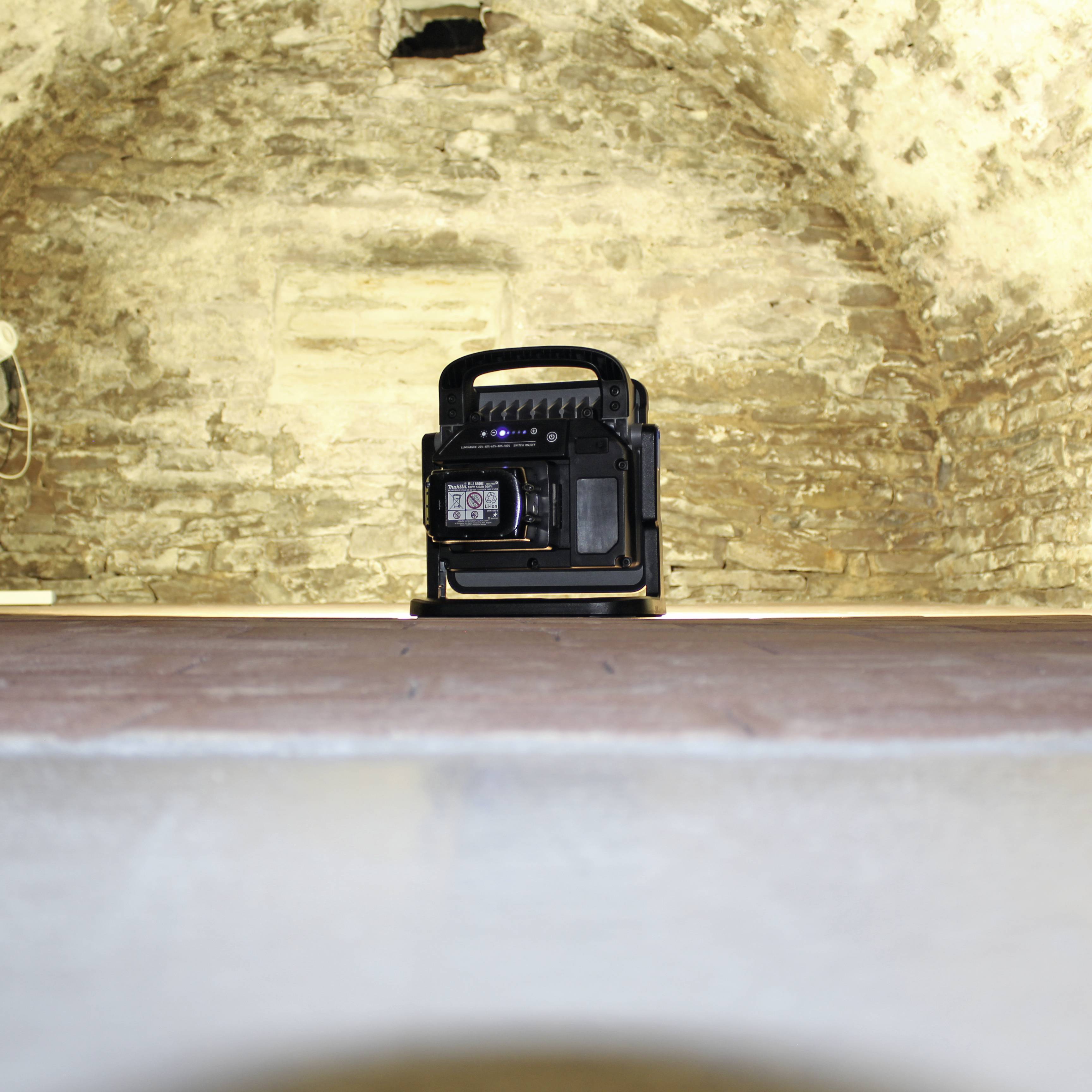 Ein tragbarer Lautsprecher steht auf einem Tisch vor einer alten Steinwand. Der Raum wirkt rustikal und historisch.