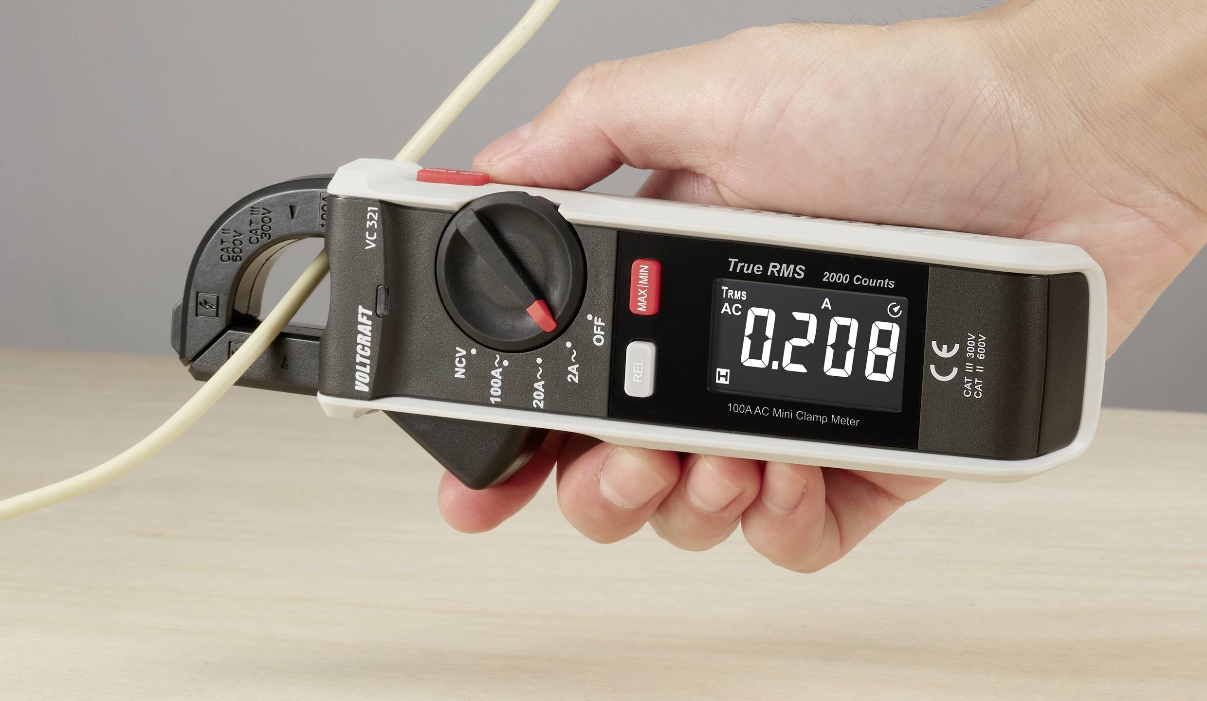 Eine Hand hält ein digitales Stromzangen-Multimeter an einem Kabel, das einen Wert von 0,208 Ampere auf dem Display anzeigt.