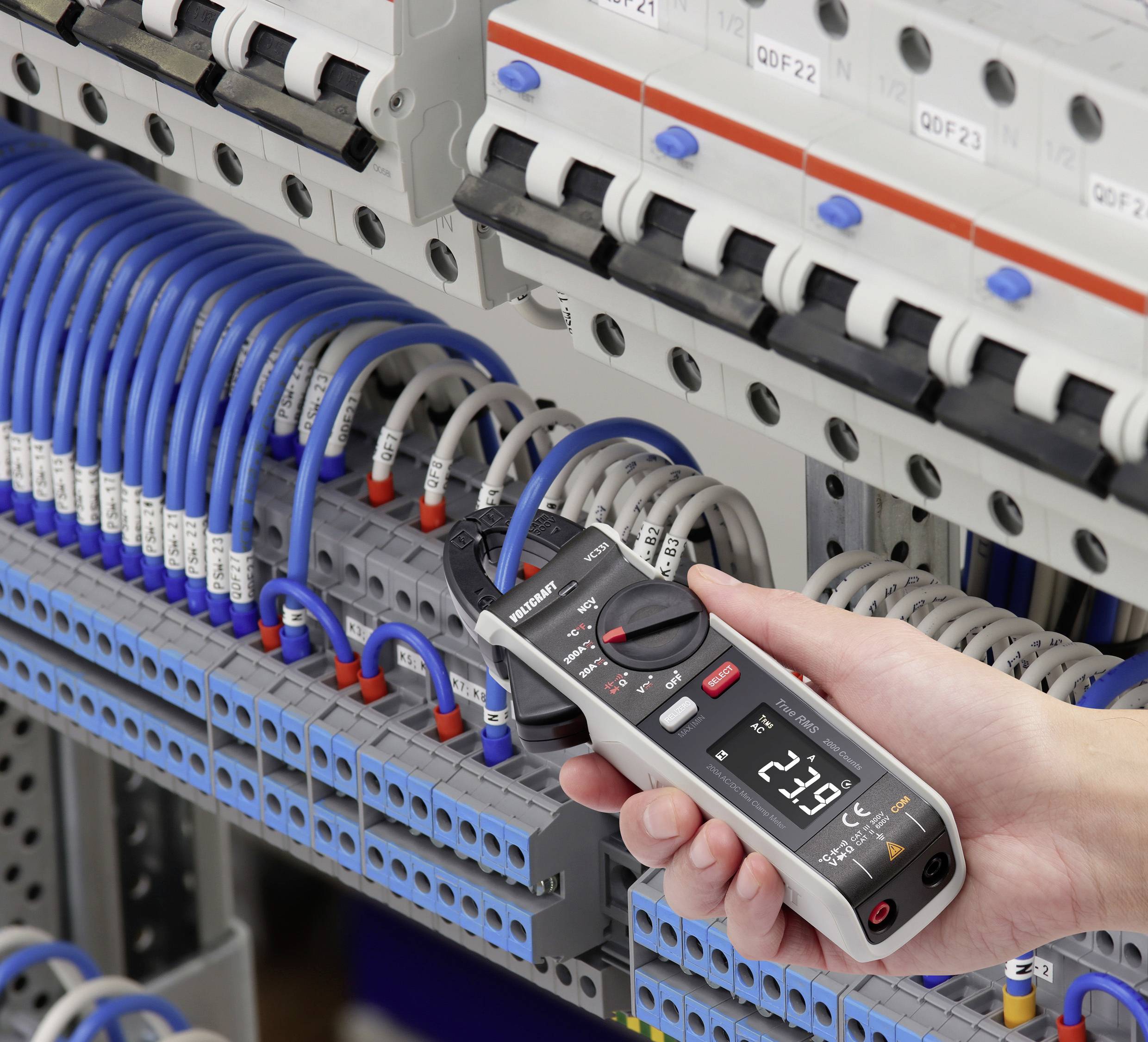 Eine Person misst die Spannung in einem Schaltschrank mit einem digitalen Multimeter. Kabel sind an verschiedenen Anschlüssen verbunden.