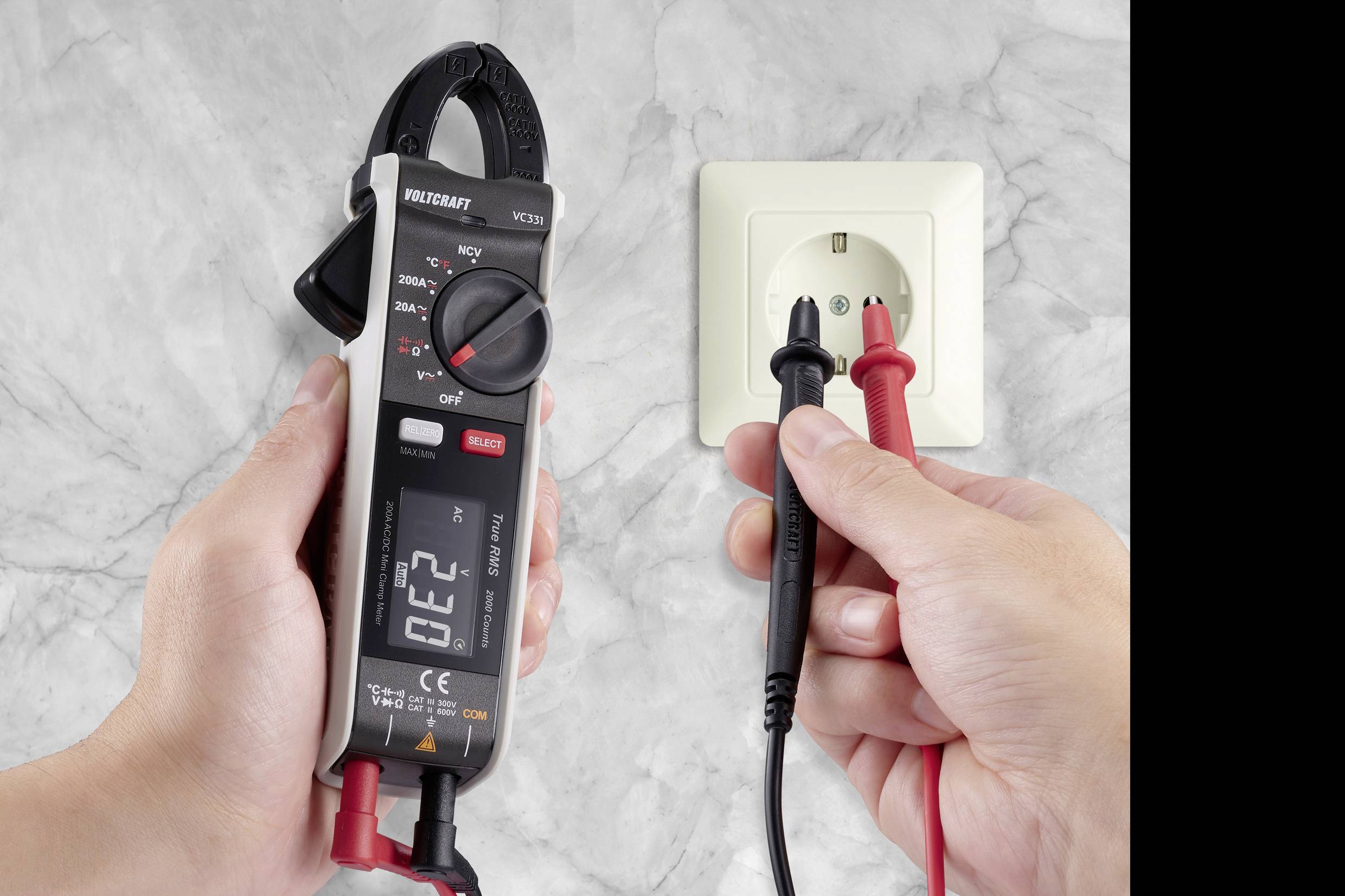 Zwei Hände testen eine Steckdose mit einem digitalen Multimeter und Prüfkabeln. Das Display zeigt '0.22' an, Wechselstrommessung.