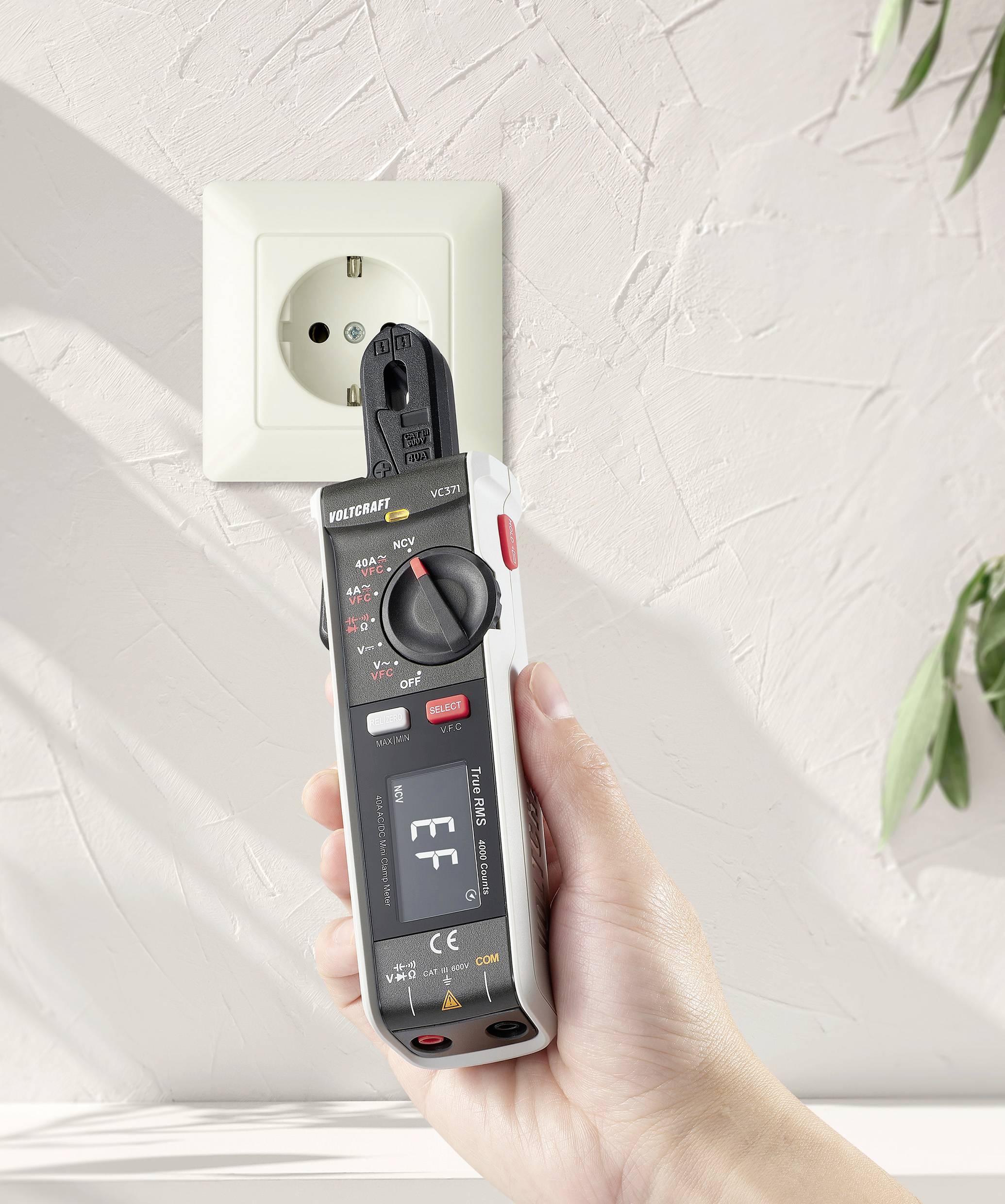 Eine Hand hält ein Multimeter am Stecker einer Wandsteckdose, um die Spannung zu prüfen.