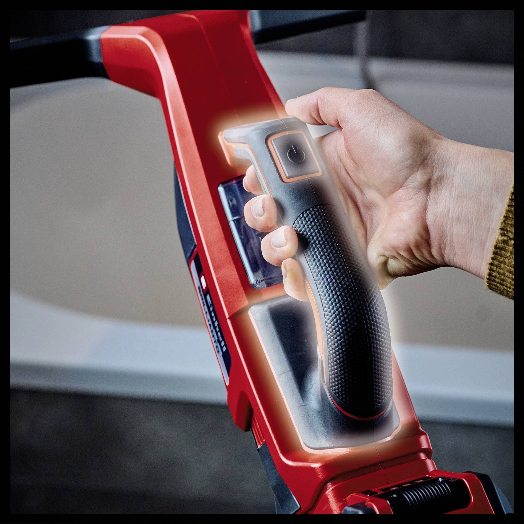Hand hält den Griff einer roten Elektrowerkzeugmaschine, vermutlich ein Bohrhammer. Fokus auf ergonomischem Design des Griffs.