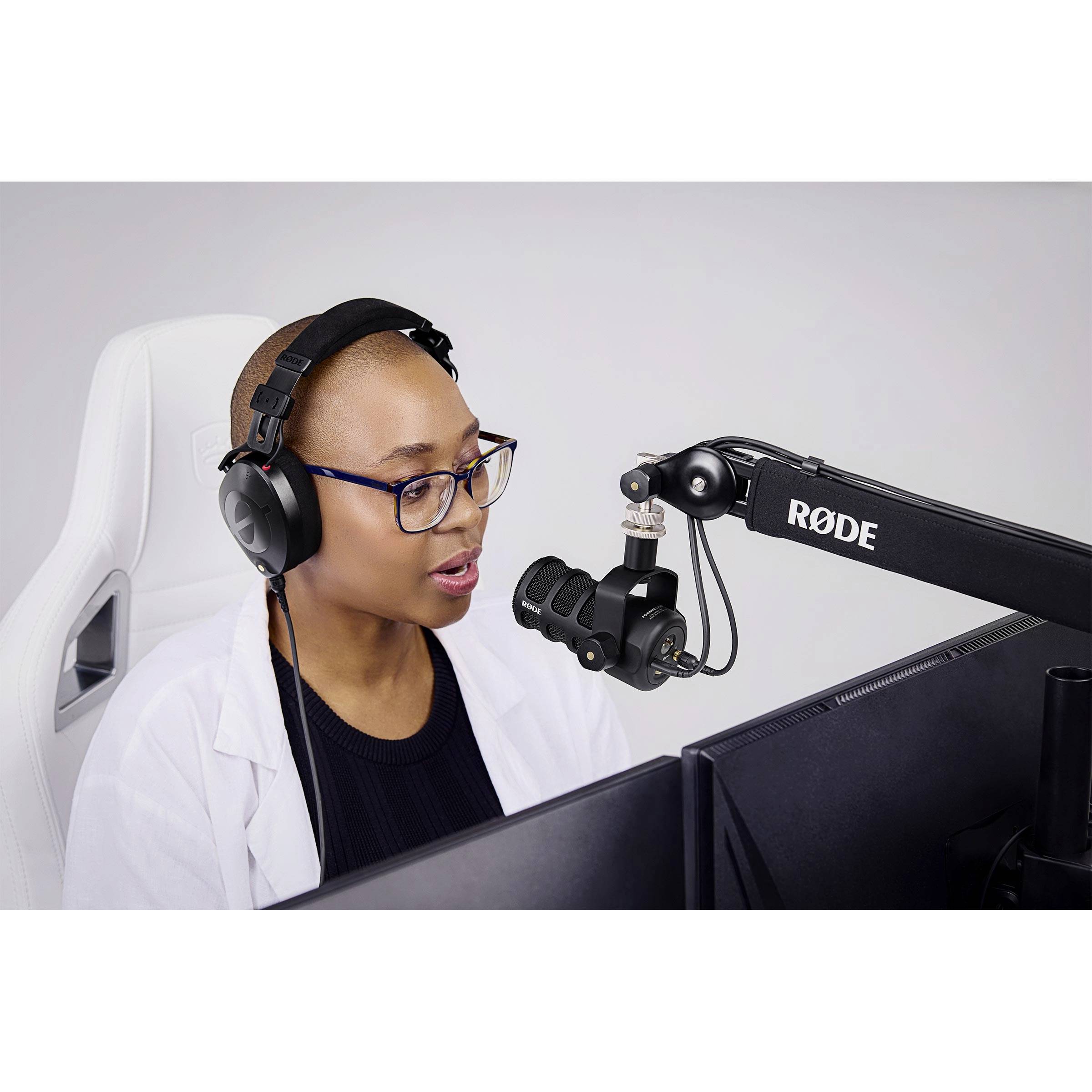 Eine Person mit Kopfhörern sitzt vor einem Mikrofon und Bildschirm und spricht. Sie scheint in einem Tonstudio oder einem ähnlichen Raum zu arbeiten.