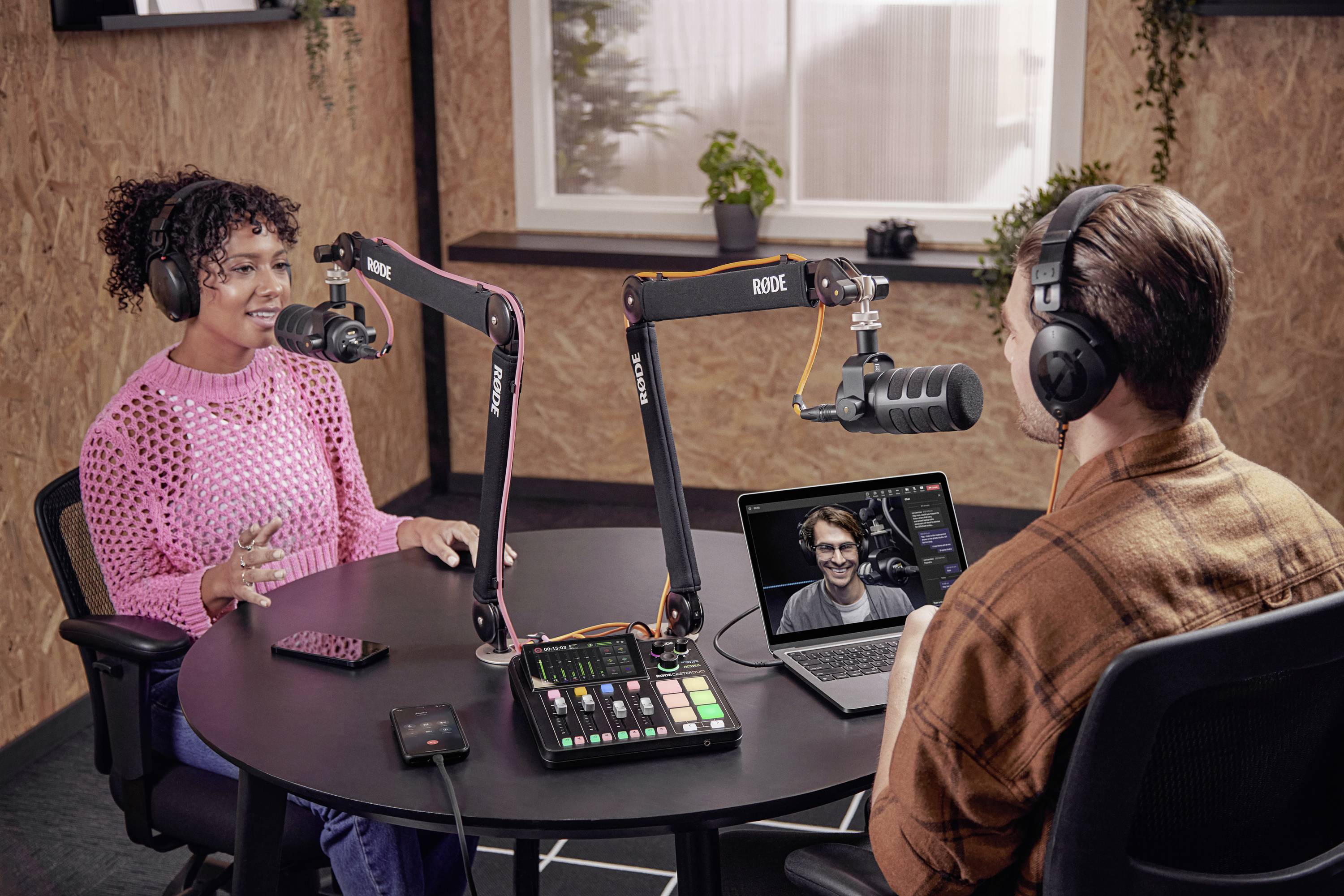 Frau und Mann mit Kopfhörern nehmen Podcast in einem Studio auf. Ein Laptop zeigt eine Videokonferenz mit einer weiteren Person.