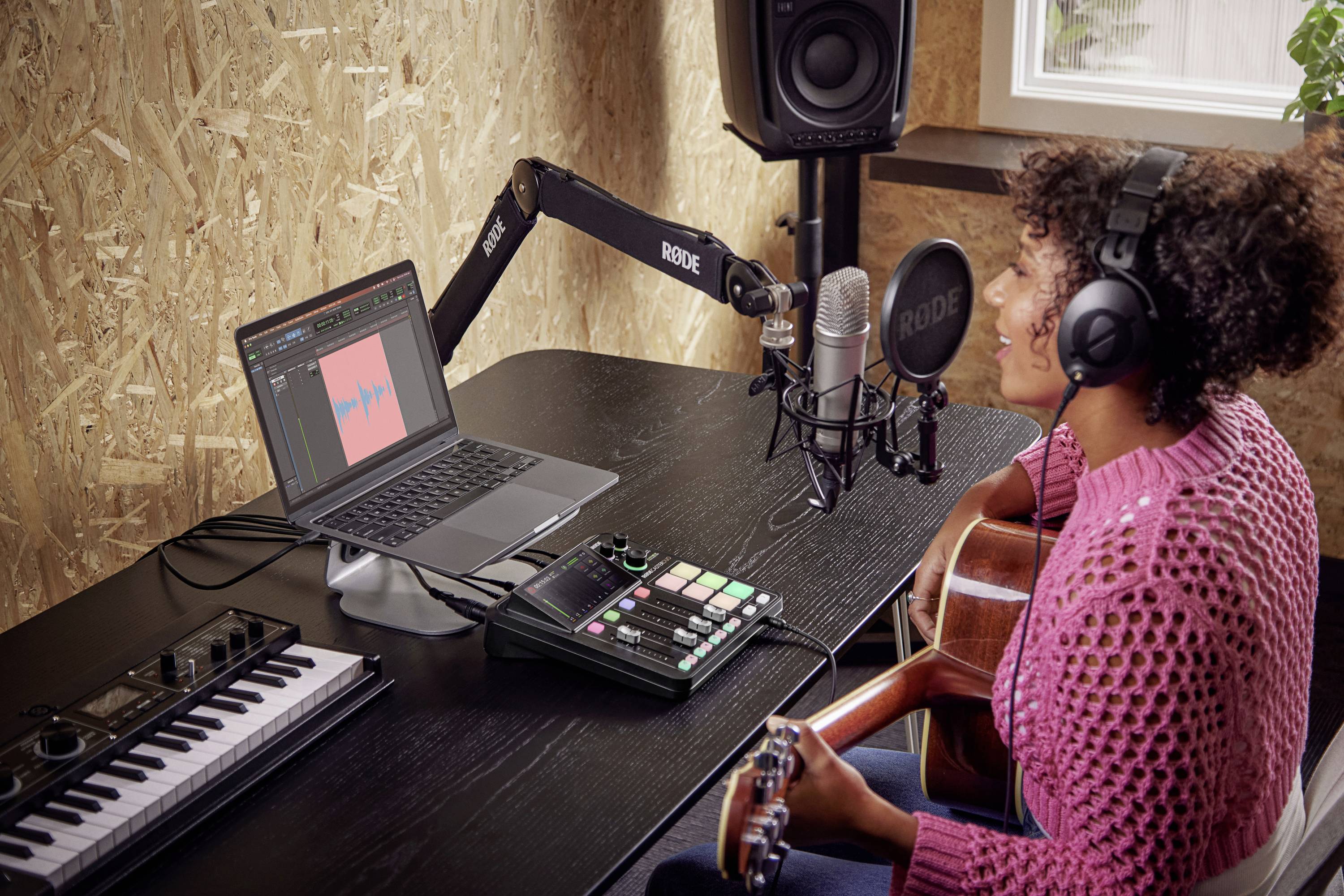 Eine Person mit Kopfhörern spielt Gitarre und nimmt Musik auf. Vor ihr Laptop mit Audiosoftware, Mikrofon und Midi-Controller.