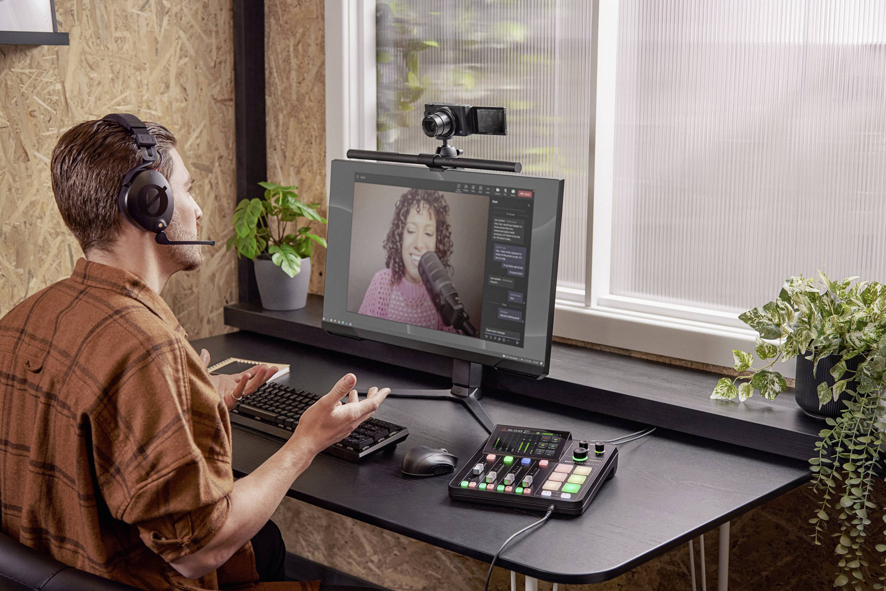 Ein Mann mit Headset sitzt an einem Tisch, bedient einen Computer und ein Mischpult. Auf dem Bildschirm eine Frau bei der Aufnahme.