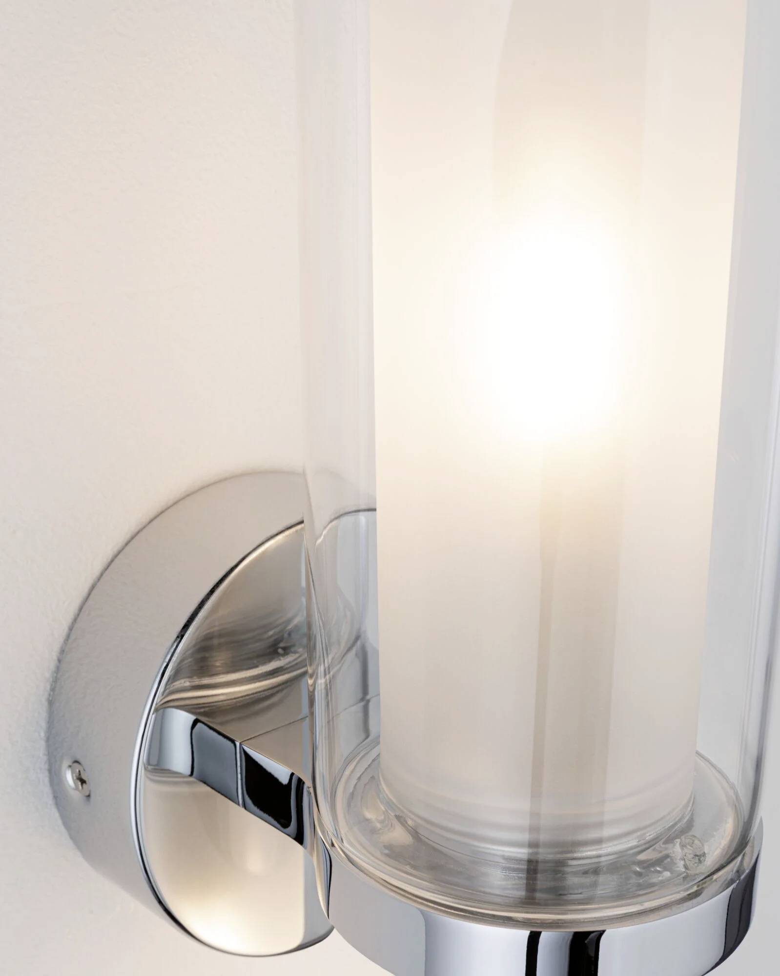Leuchtende Wandlampe mit modernem Design, zylindrischer Glasabdeckung und silbernem Sockel, an einer hellen Wand montiert.