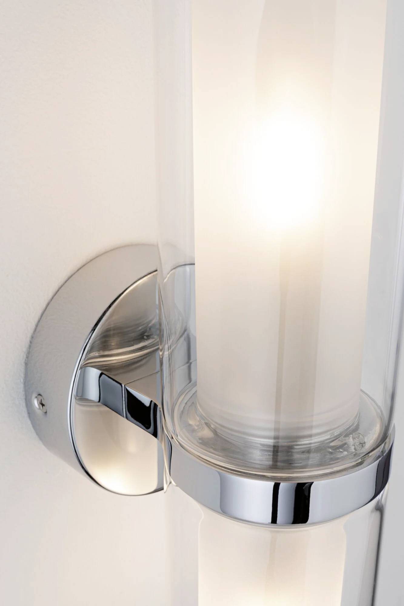 Wandleuchte mit glänzendem, verchromtem Halter und zylindrischem Milchglas, strahlt warmes Licht aus.