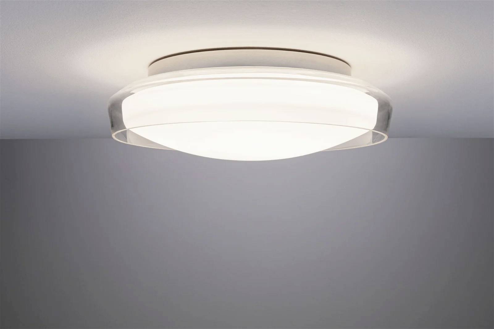 Moderne Deckenleuchte aus klarem Glas, leuchtet hell an einer weißen Decke und sorgt für gleichmäßige Raumbeleuchtung.