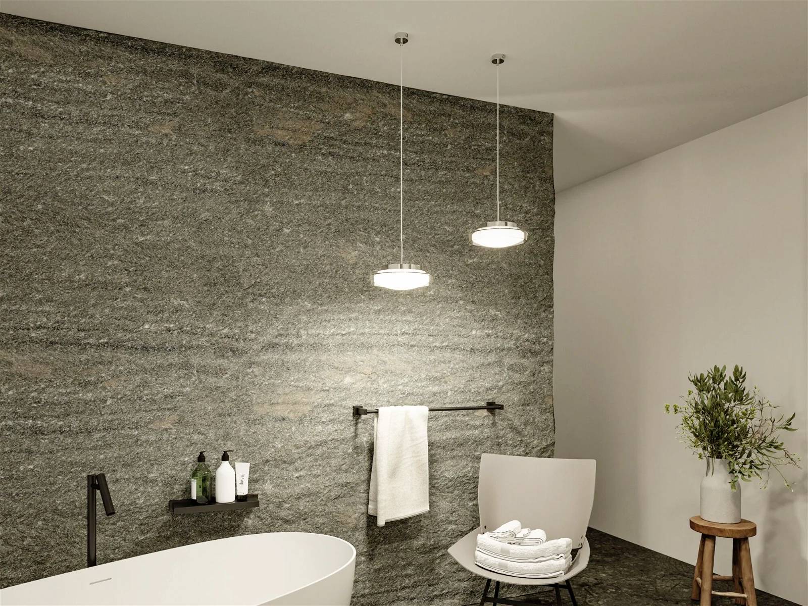 Badezimmer mit freistehender Badewanne, zwei hängende Lampen und Natursteinwand. Ein Stuhl mit Handtüchern steht daneben.