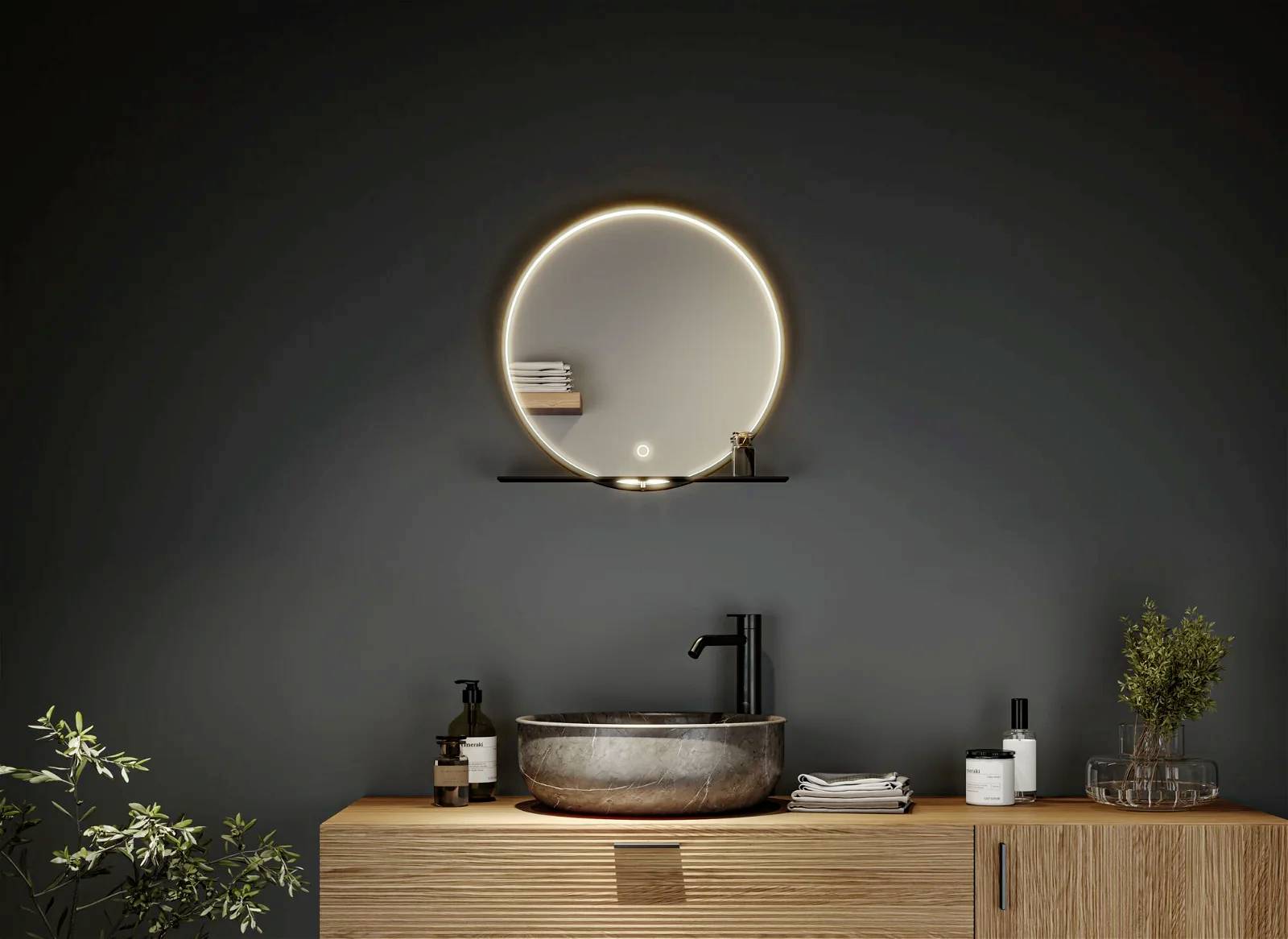 Ein modernes Badezimmer mit einem runden, beleuchteten Spiegel über einem Waschbecken aus Stein. Pflanzen und Seifenspender sind dekorativ platziert.