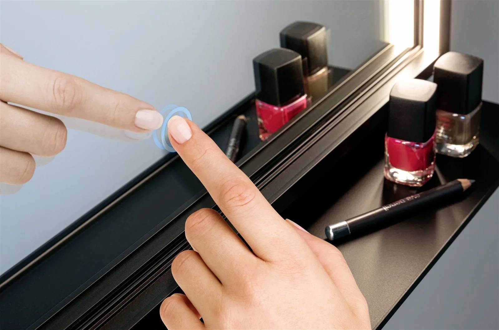Eine Person berührt einen beleuchteten Spiegel. Im Regal darunter stehen Nagellack in Rot- und Nudetönen sowie ein schwarzer Kajalstift.