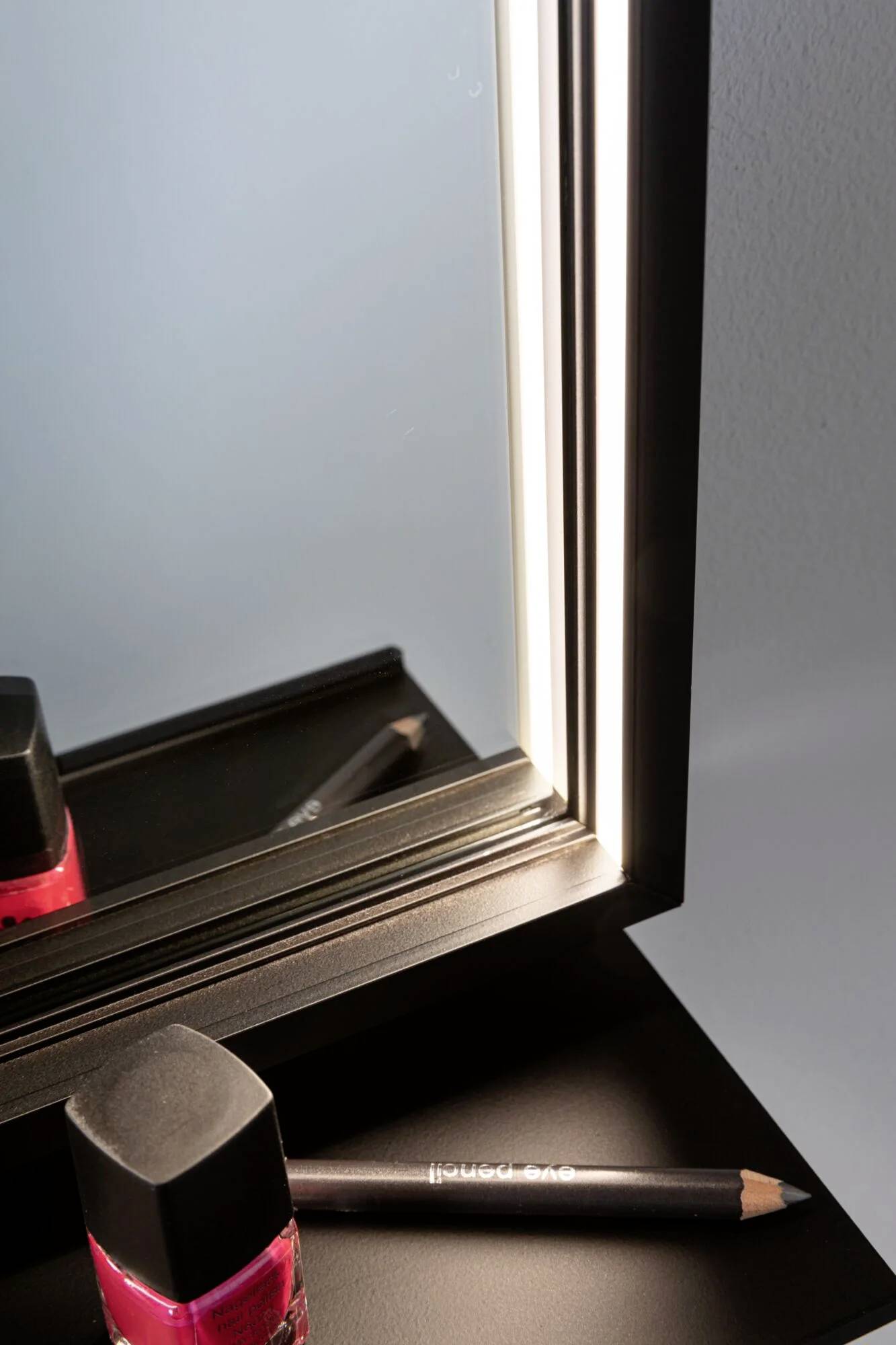 Ein beleuchteter Schminkspiegel neben einem Lippenstift und einem Kajalstift auf einer schwarzen Oberfläche.