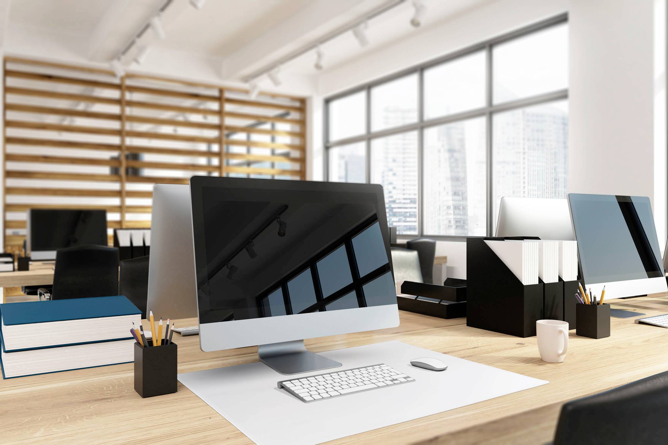 Moderne Bürofläche mit Schreibtischen, Monitoren und Stadtansicht im Hintergrund. Helle und geräumige Umgebung.