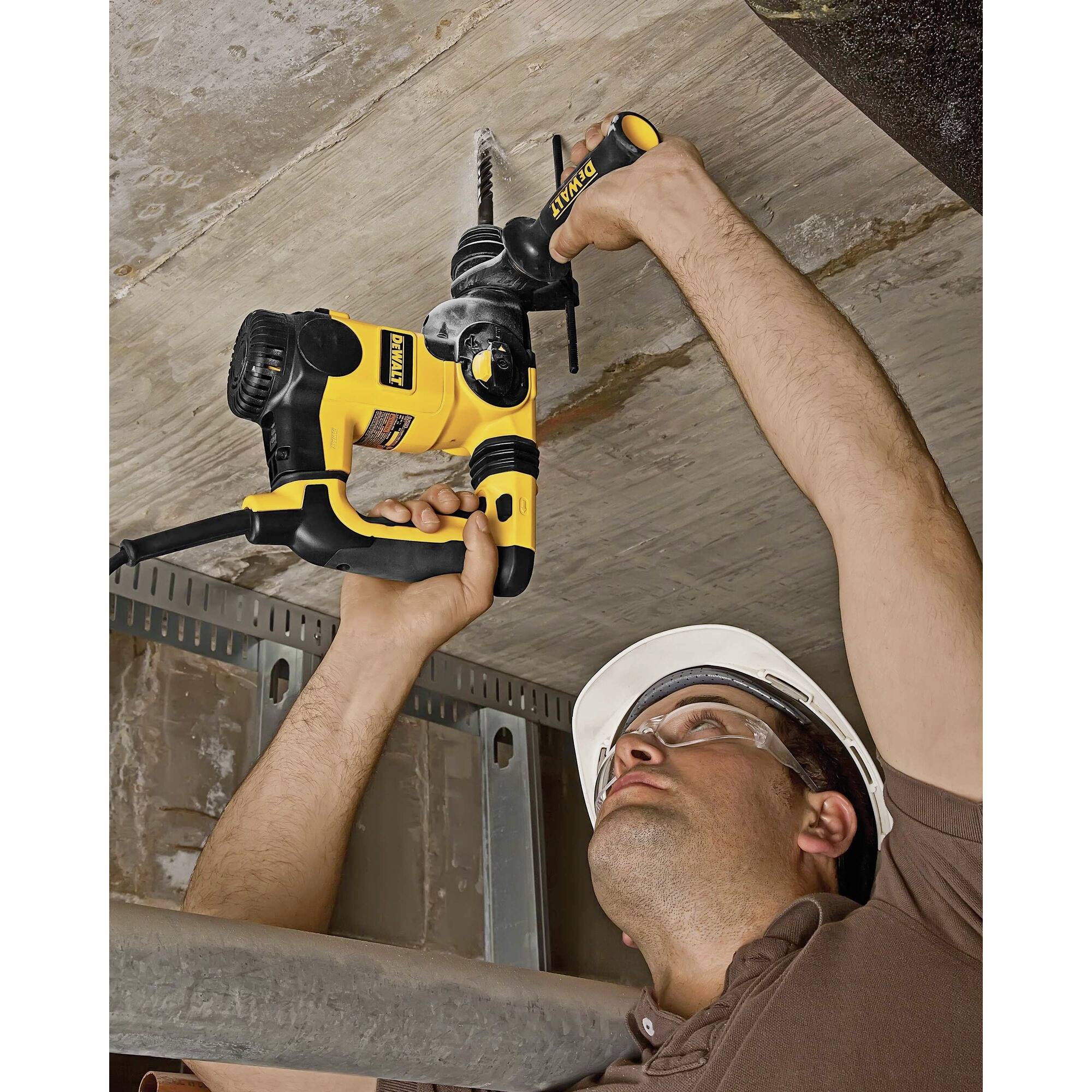 Eine Person mit Schutzhelm bohrt mit einer elektrischen Schlagbohrmaschine in eine Betonwand an der Decke.