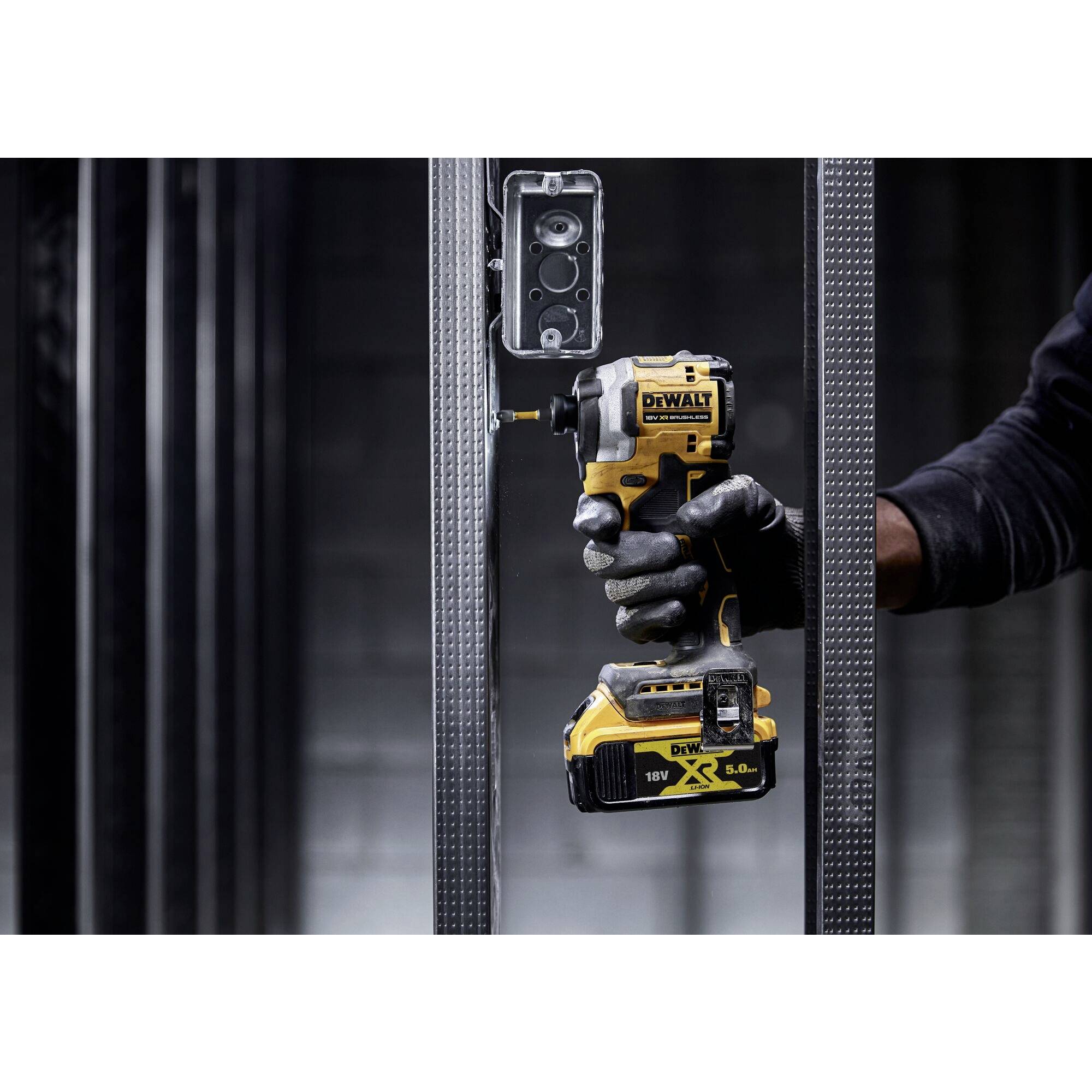 Eine Person befestigt mit einem Akkuschrauber ein Elektrogehäuse an einem Metallständer. Werkzeug und Arbeitsvorgang sind im Fokus.