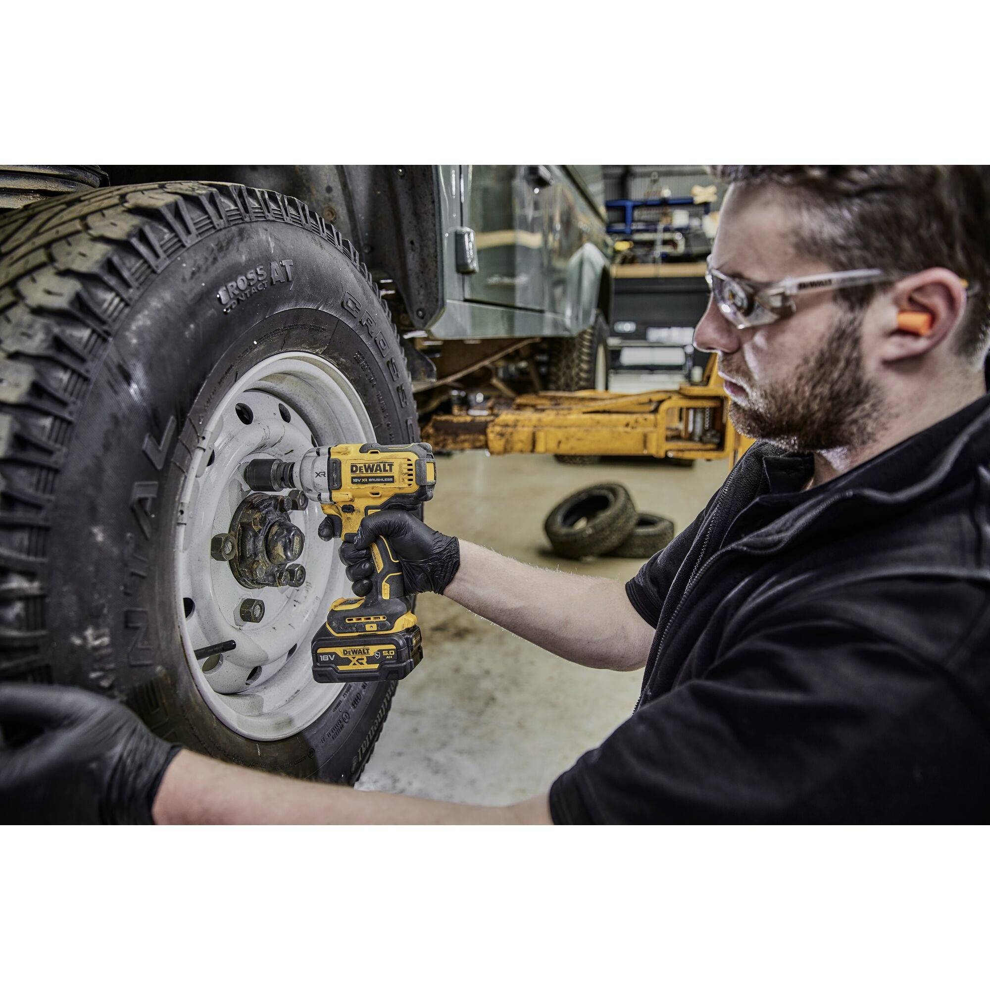 Ein Mann benutzt einen elektrischen Schraubenschlüssel, um die Radmuttern eines Fahrzeugs zu lösen. Er trägt Schutzbrille und Handschuhe.