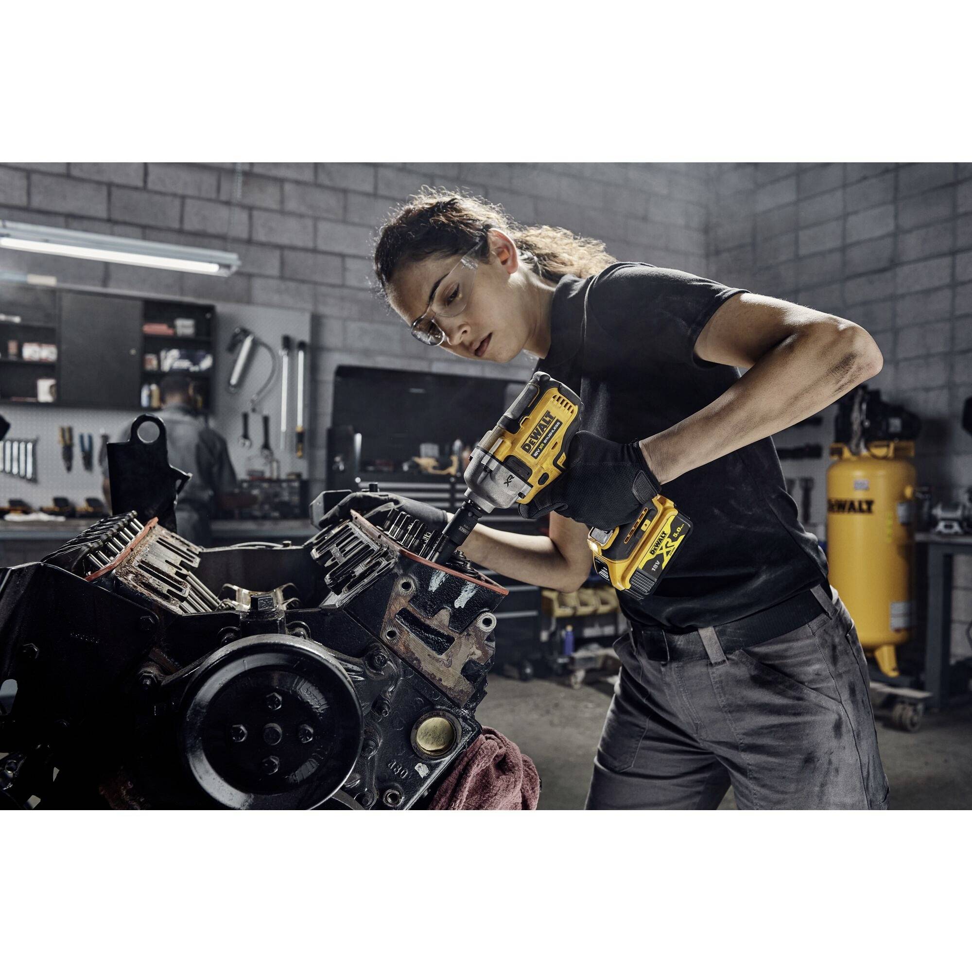 Eine Person in einer Werkstatt arbeitet konzentriert mit einem elektrischen Werkzeug an einem großen Motor. Im Hintergrund stehen Werkzeuge und Geräte.