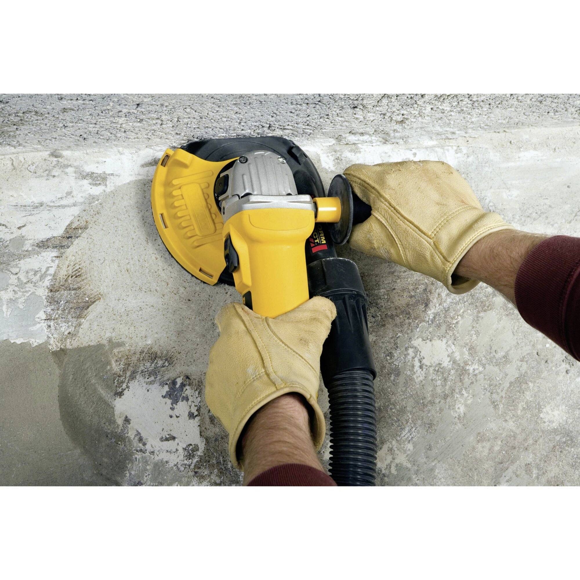 Eine Person schleift eine Betonfläche mit einem Winkelschleifer. Handschuhe schützen die Hände, während Staub abgesaugt wird.