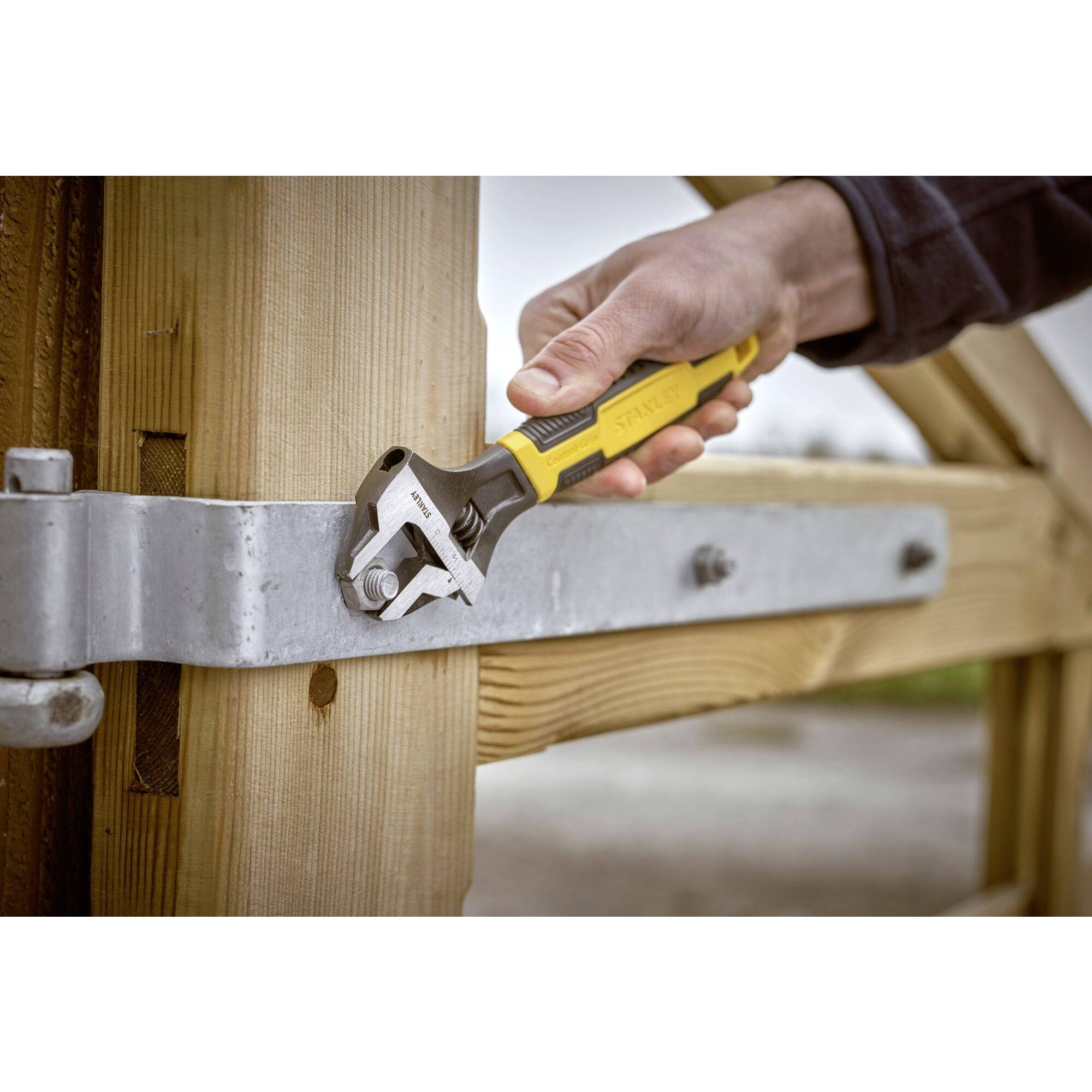 Hand zieht Schraube mit verstellbarem Schraubenschlüssel an, befestigt Metallbeschlag an Holztorrahmen im Freien.