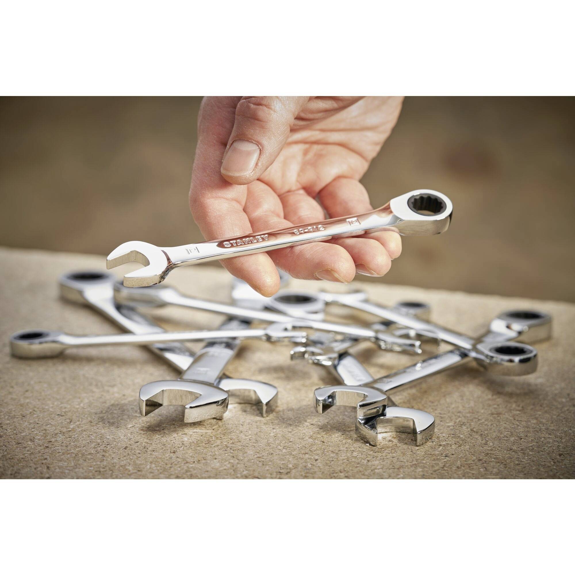Eine Hand hält einen Ringschlüssel über mehrere verstreute Ringschlüssel auf einem Tisch.