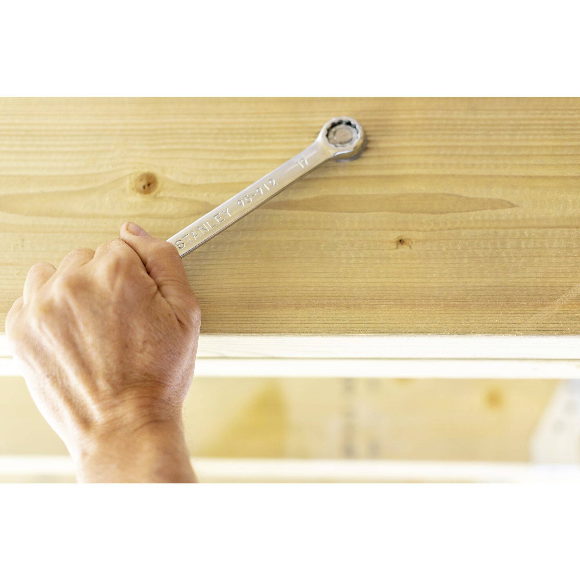 Eine Hand hält einen Schraubenschlüssel und dreht eine Schraube in einem Holzbalken fest.