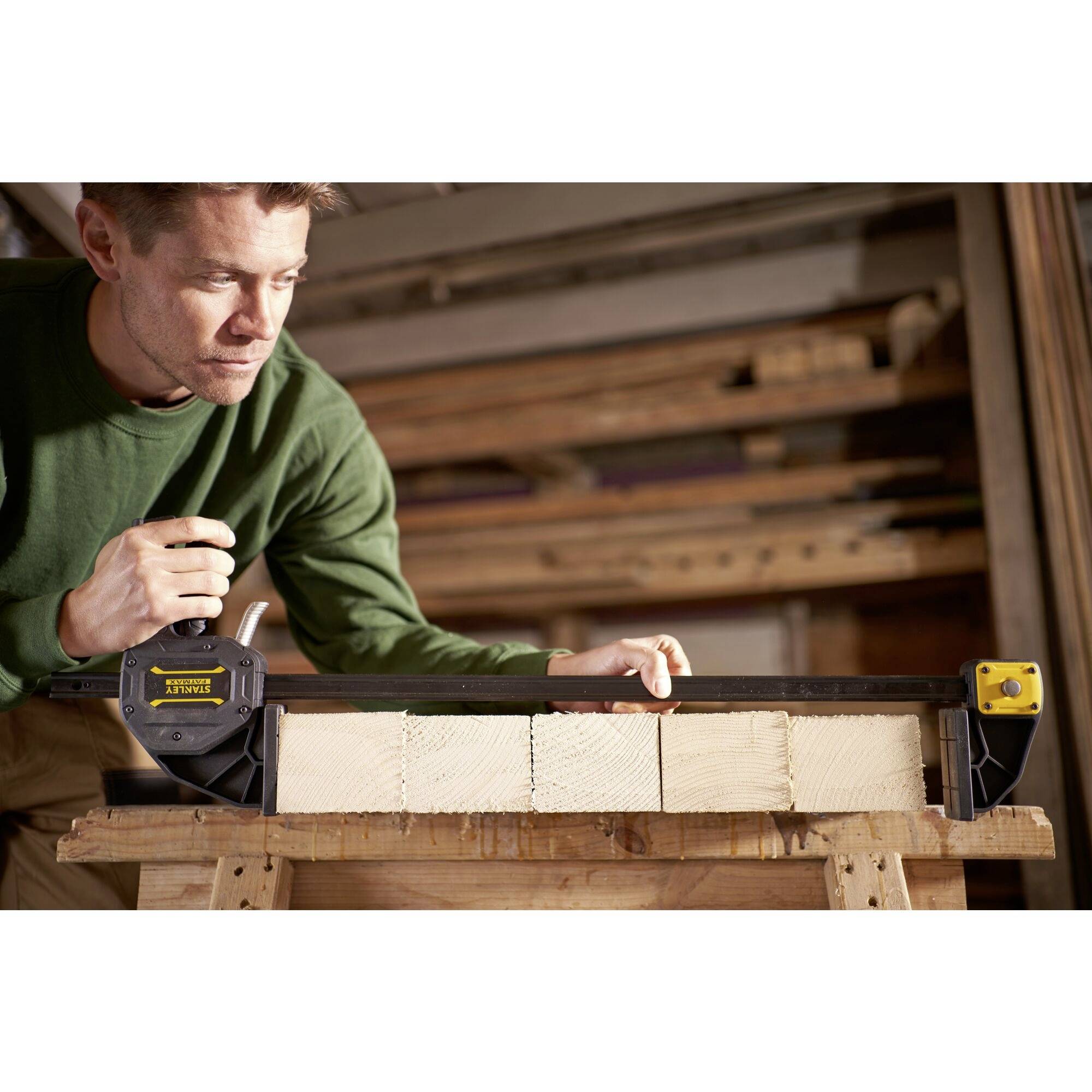 Ein Mann in einer Werkstatt misst mit einem elektromagnetischen Gerät die exakte Länge einer Holzlatte auf einem Arbeitstisch.