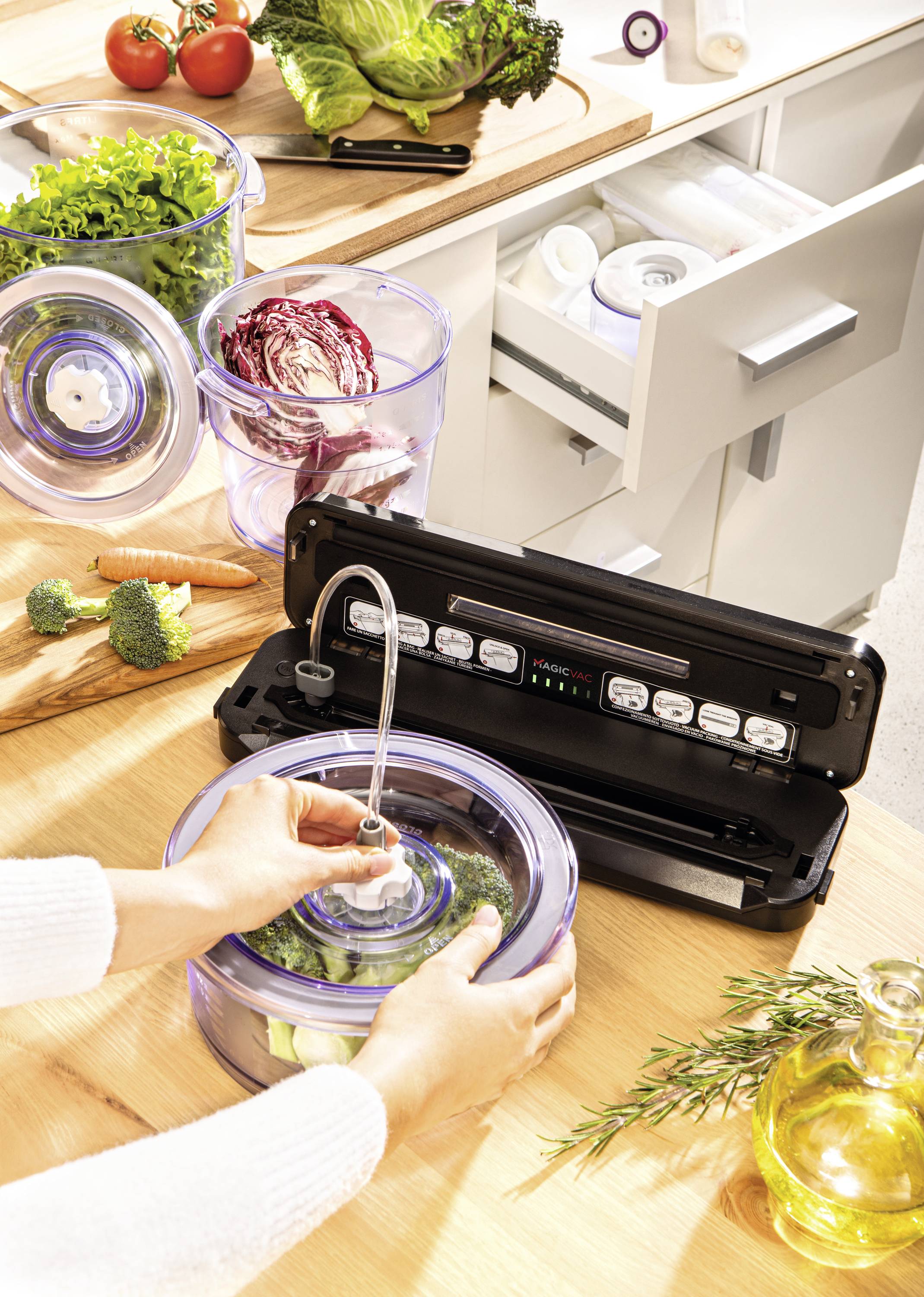 Person vakuumiert Gemüse in einem Behälter mit einer Vakuumiermaschine. Auf der Arbeitsfläche liegen frisches Gemüse und Küchenutensilien.