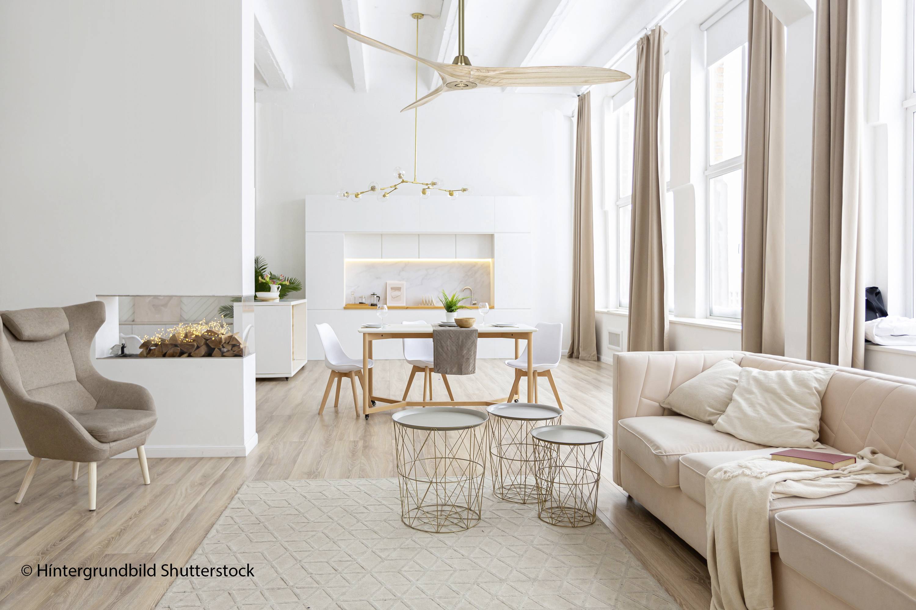 Helles, modernes Wohnzimmer mit beigem Sofa, Kaffeetischen und offener Küche im Hintergrund. Große Fenster lassen viel Licht herein.