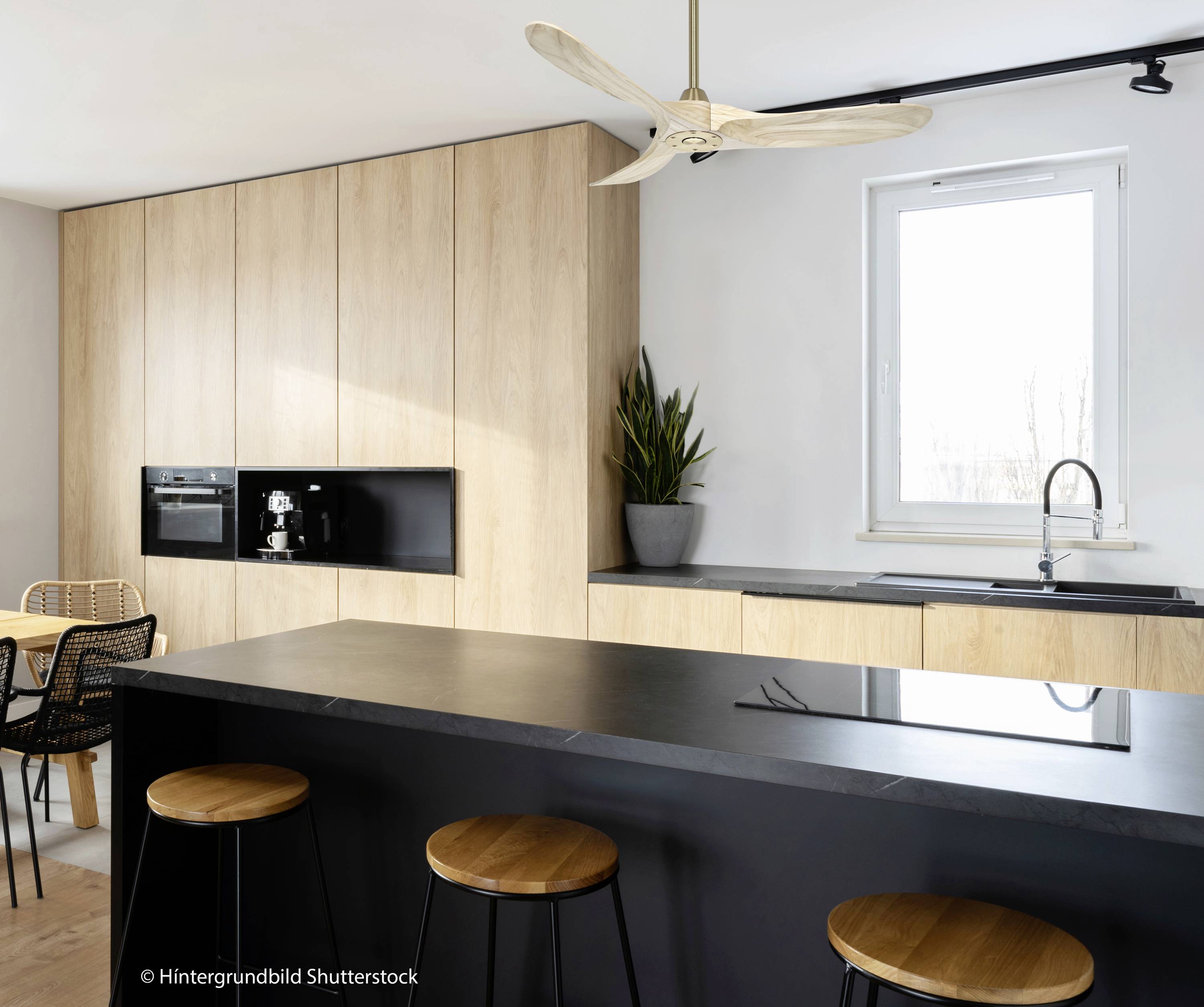 Moderne Küche mit schwarzer Arbeitsplatte und Holzdekor. Schwarze Hocker vor der Insel, Pflanzen und Fenster im Hintergrund.