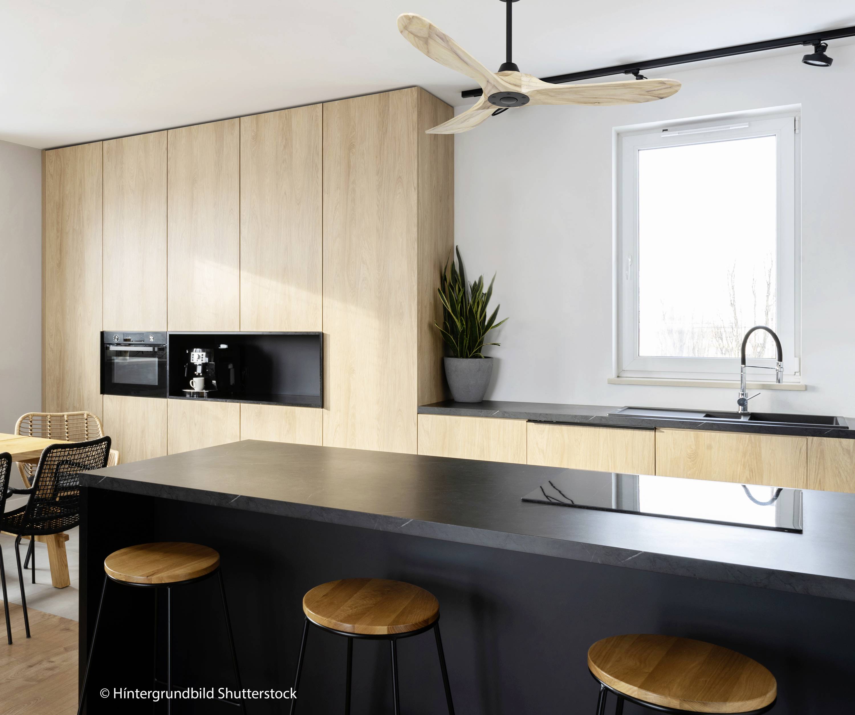 Moderne Küche mit schwarzer Arbeitsplatte, Holzschränken, kleinem runden Tisch und Stühlen. Ein großes Fenster sorgt für Helligkeit.