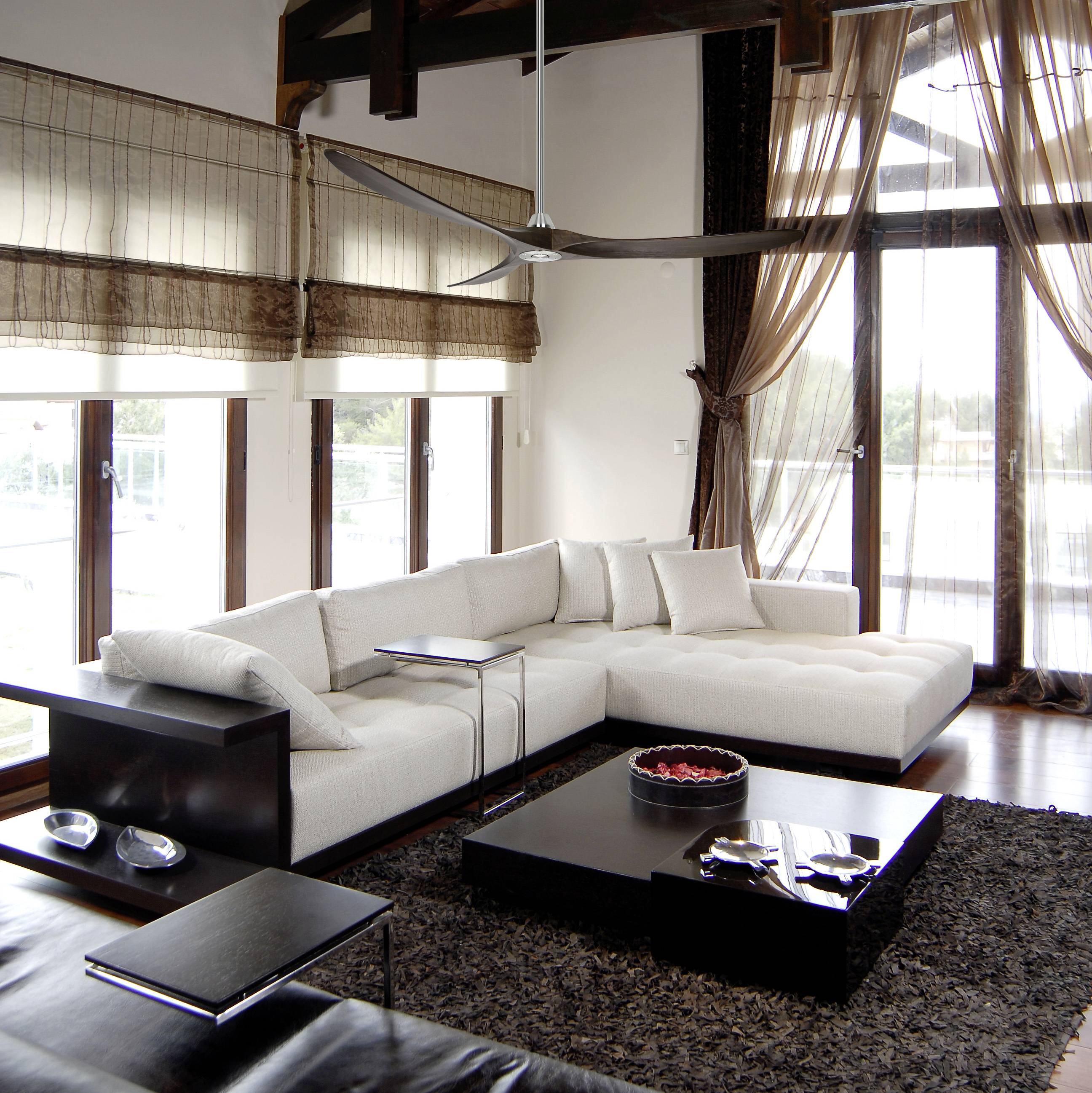 Ein modernes Wohnzimmer mit einem großen, weißen Ecksofa, Couchtisch und Teppich. Große Fenster lassen viel Licht herein.