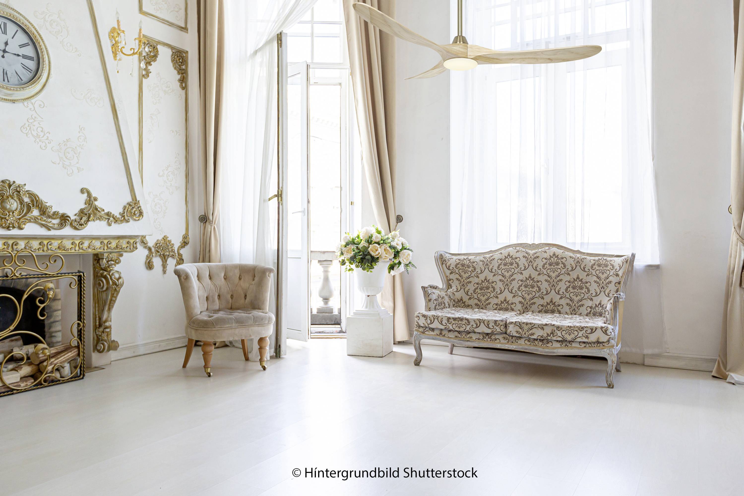 Heller, eleganter Raum mit antikem Sofa, Sessel, Kamin, Blumenstrauß auf weißem Boden vor großen Fenstern.