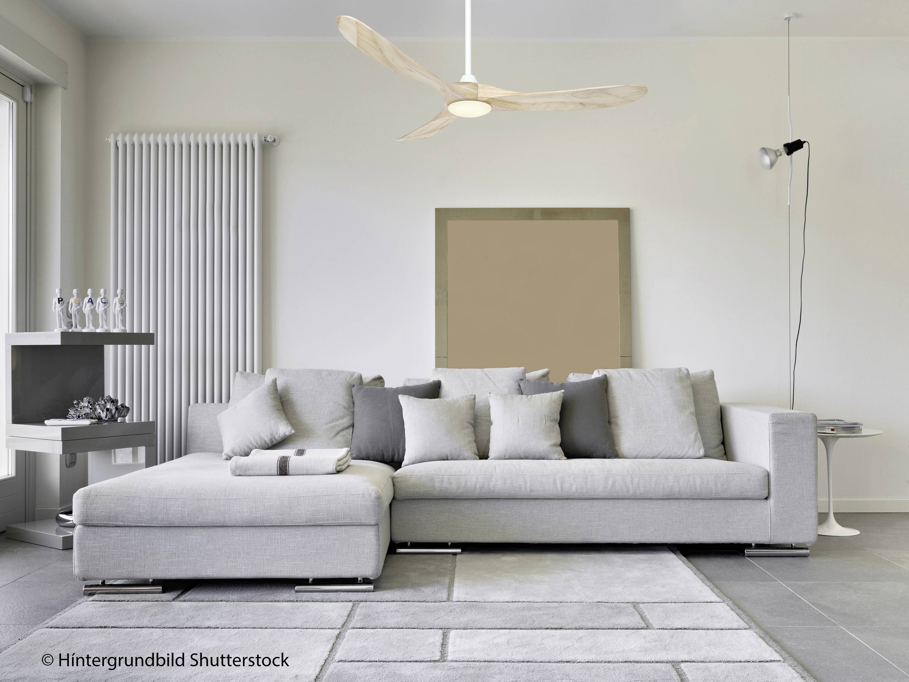 Modernes Wohnzimmer mit grauem Ecksofa, dekorativen Kissen, Teppich, hellem Holzboden, Deckenventilator und minimalistischer Beleuchtung.