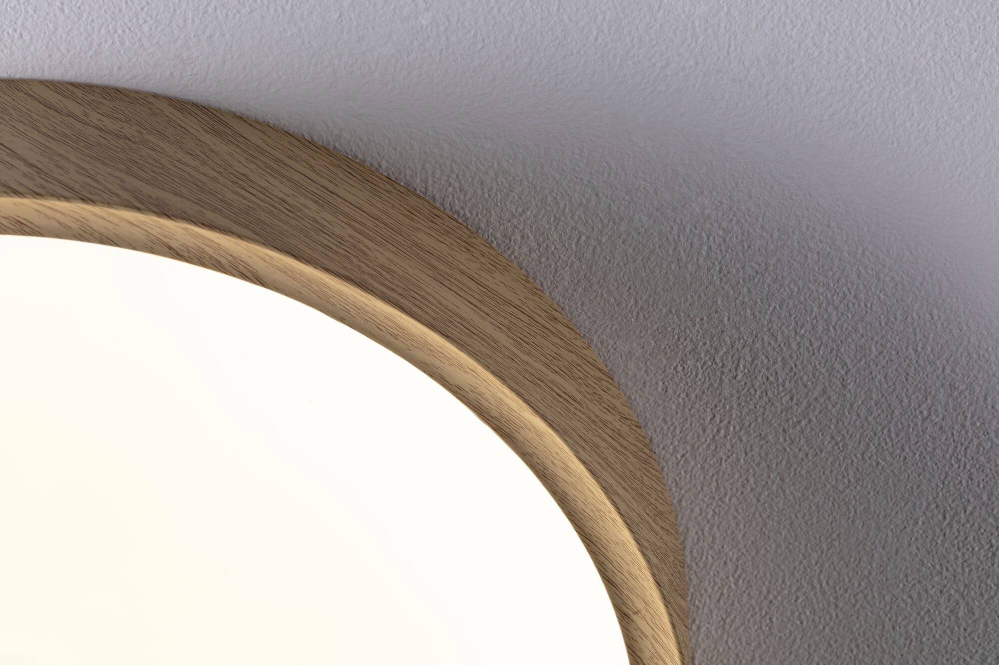 Ein Teil einer runden Lampe mit Holzverkleidung an einer weißen Wand, zeigt modernes Design und Beleuchtungselement.