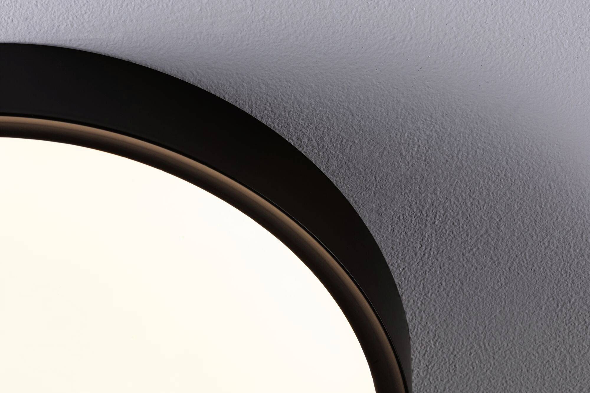 Ein Teil einer runden Deckenleuchte, die an einer weißen, strukturierten Decke installiert ist. Die Lampe wirft ein weiches, diffuses Licht.