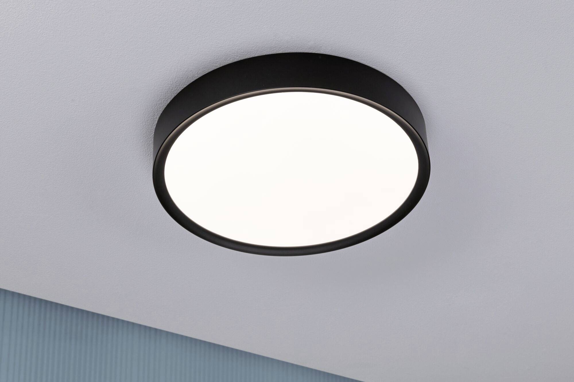 Eine runde Deckenleuchte mit schwarzem Rahmen, die an einer weißen Decke montiert ist, leuchtet hell und gleichmäßig im Raum.